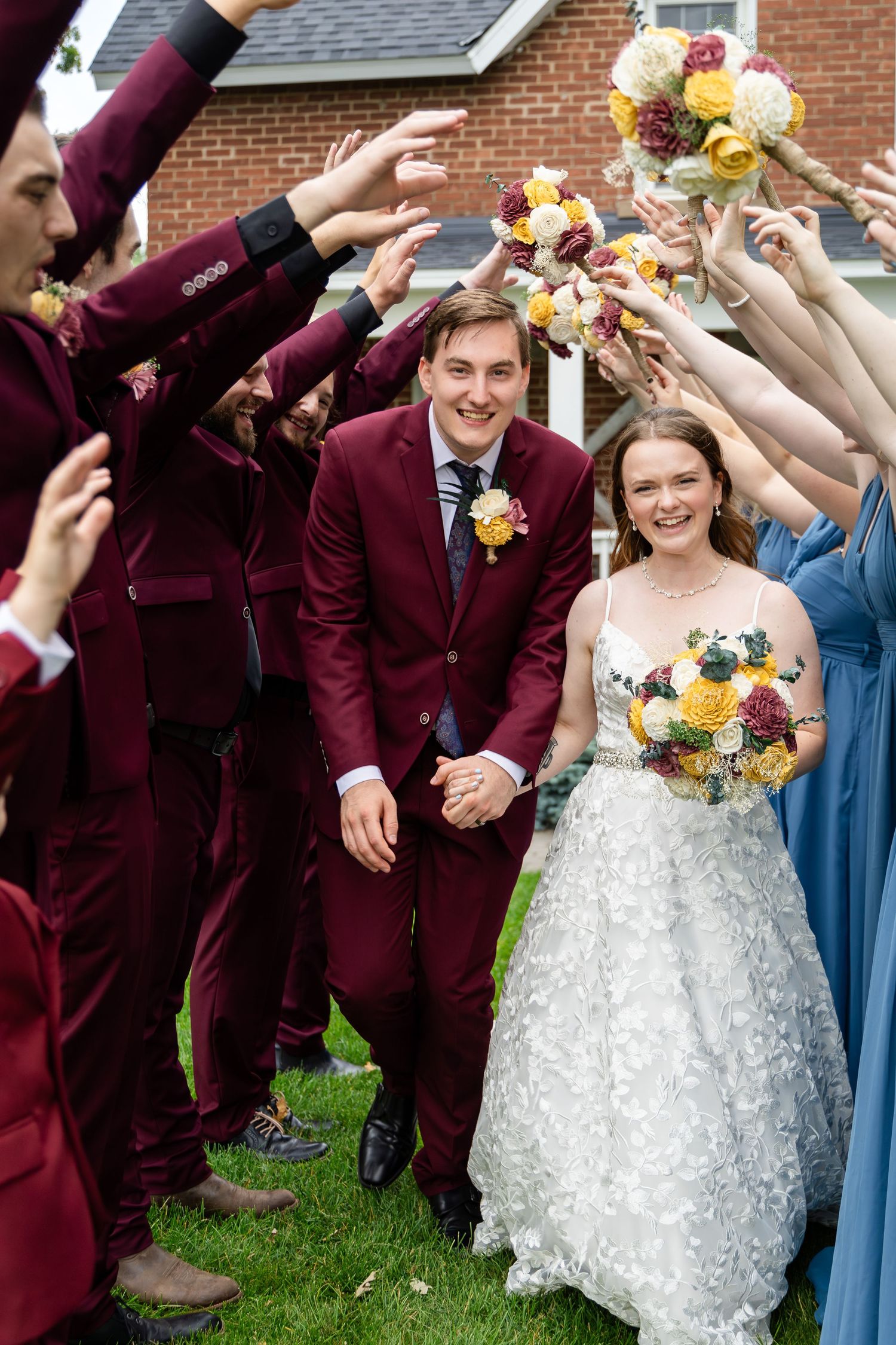 Joyful wedding party celebrates outdoors with burgundy suits and white gown.