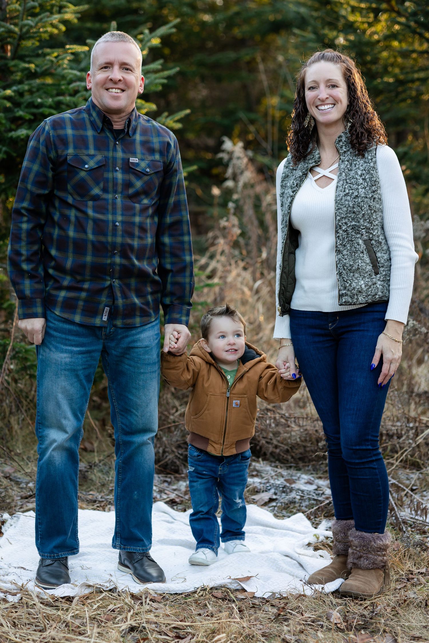 Family group stands together in casual winter attire on snowy ground.