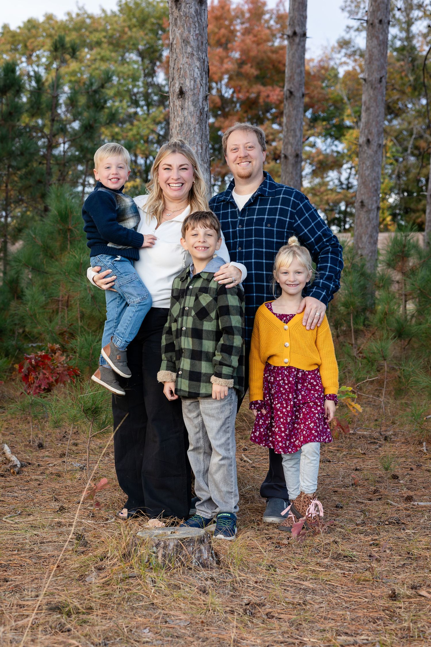 Playful family portrait with children in colorful outfits among pine trees.