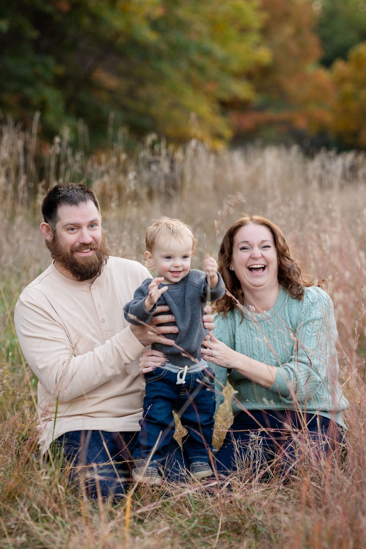 Family sitting together in tall autumn grass sharing candid laughs and embraces.