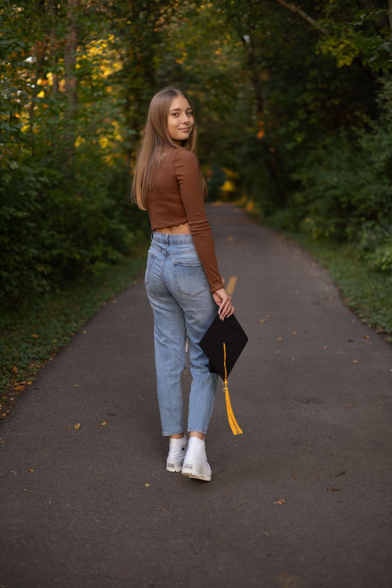 Person walking on autumn path wearing brown sweater and light jeans.