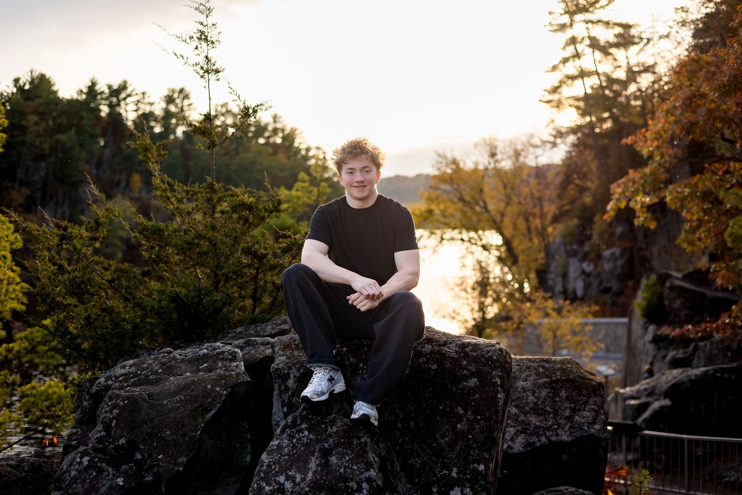 Someone sits on large rocks at sunset with a lake and forest in the background during golden hour.
