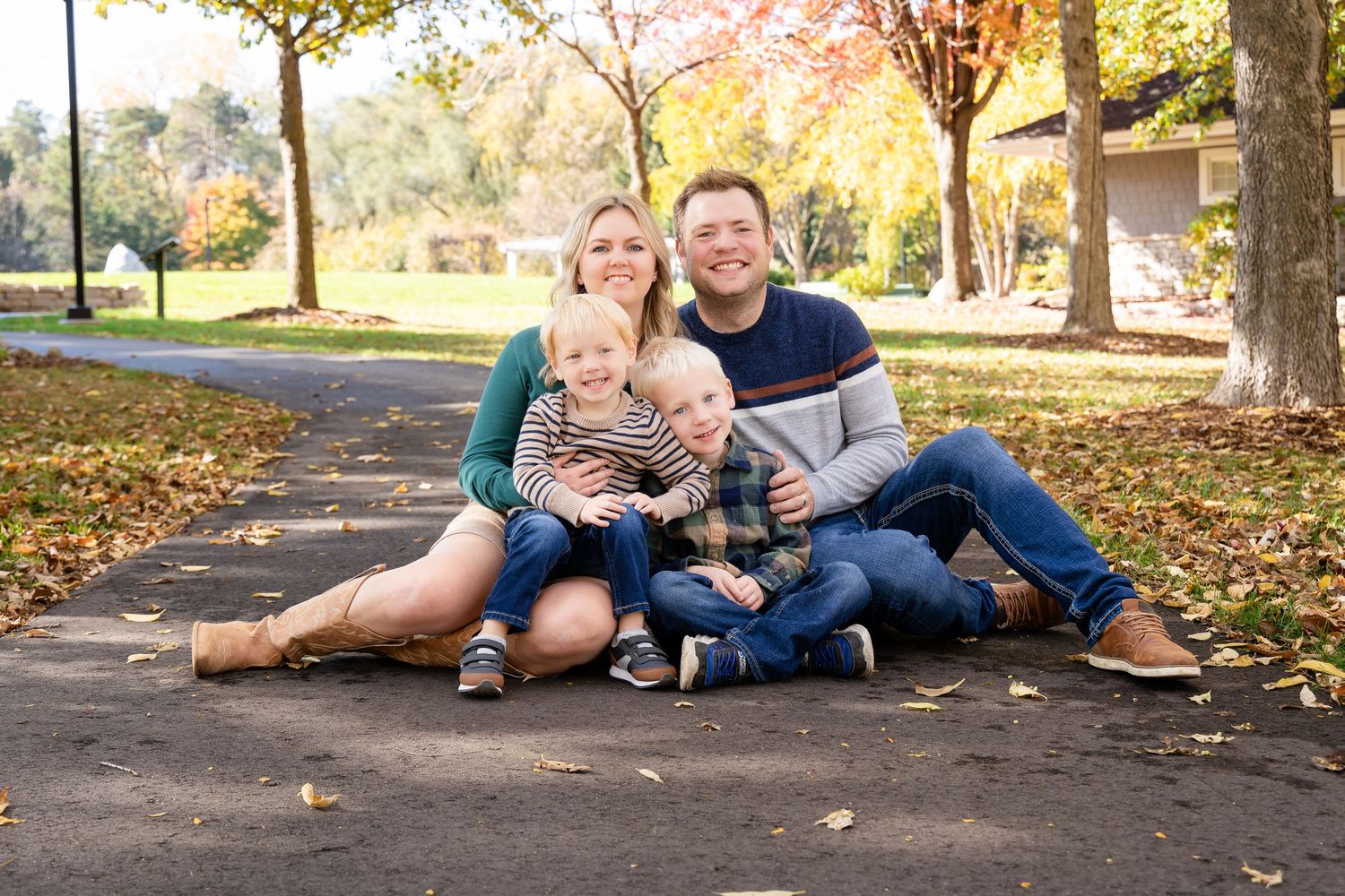 Family relaxing together on ground during autumn photoshoot in park.