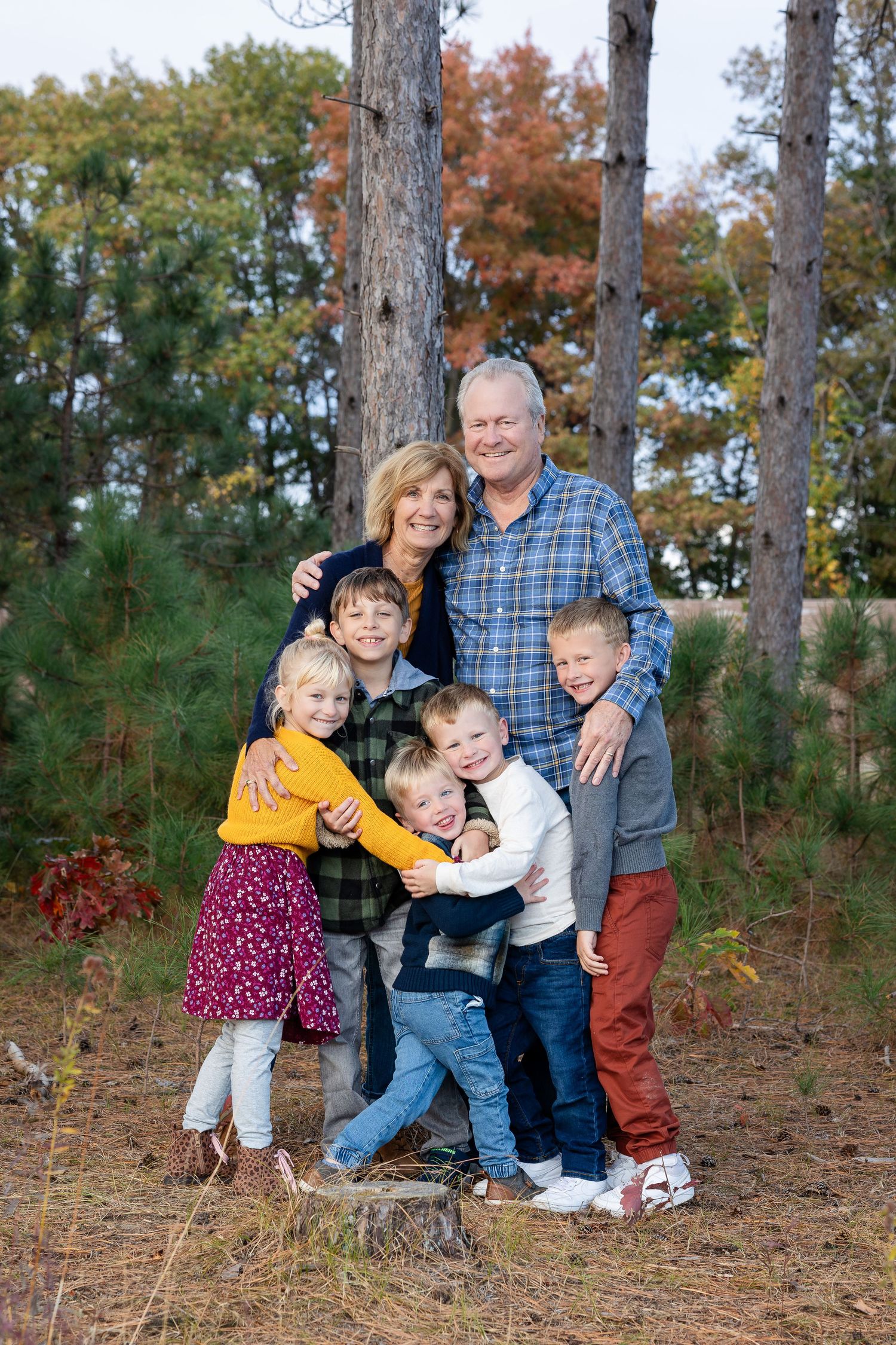 Family sitting together on pine needles for a casual outdoor portrait.