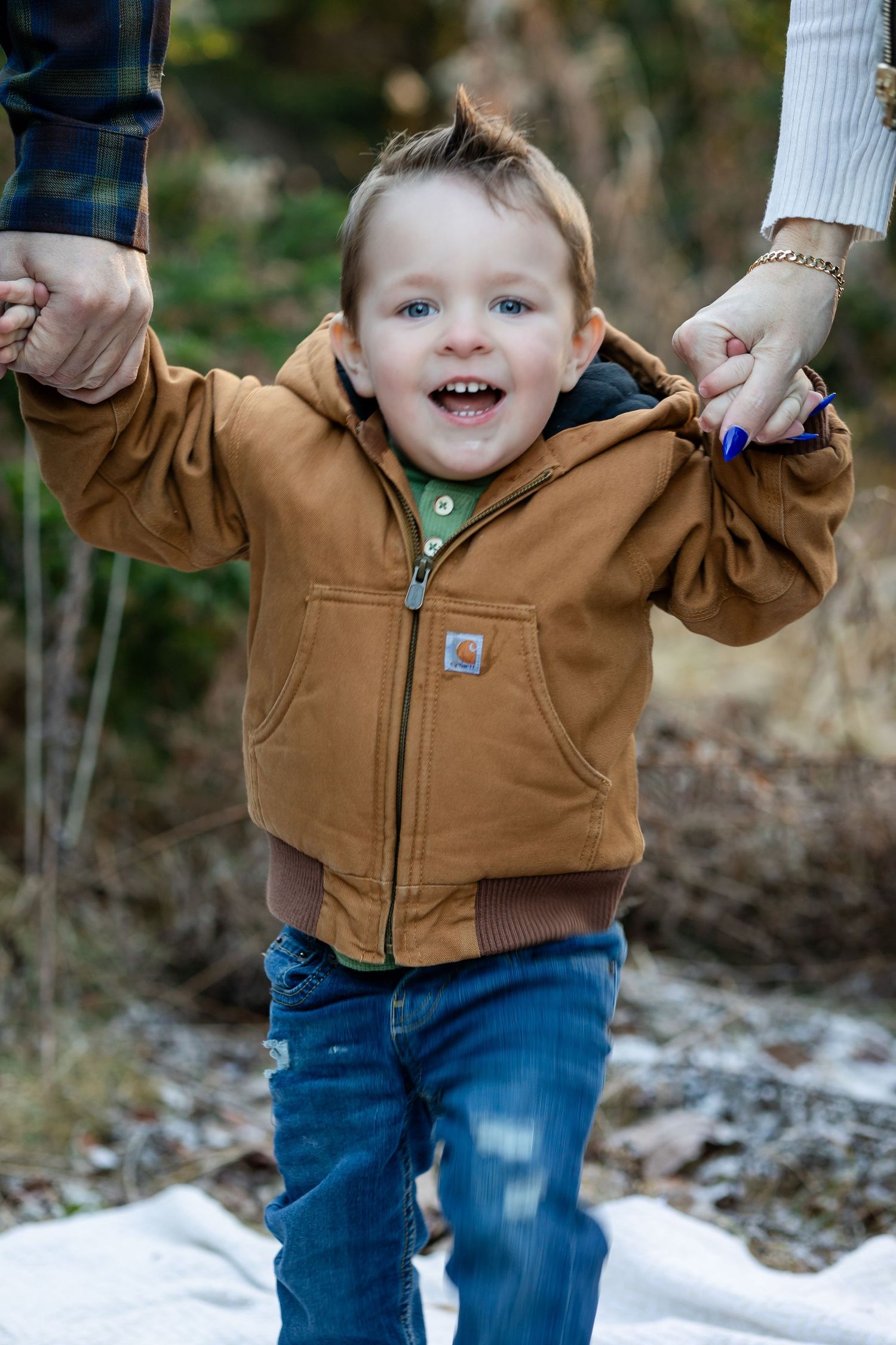 Small child in brown Carhartt jacket plays in the snow with joyful expression.
