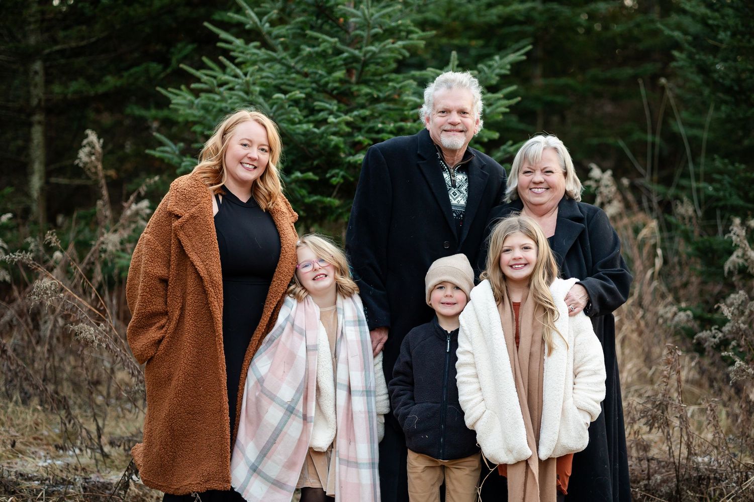 Family wearing cozy winter coats poses together in a snowy forest setting.
