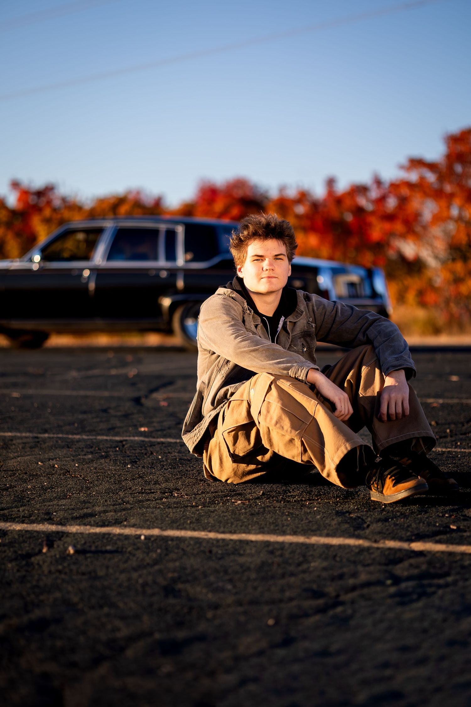 A relaxed outdoor portrait with a classic car and vibrant fall colors in the background at sunset.