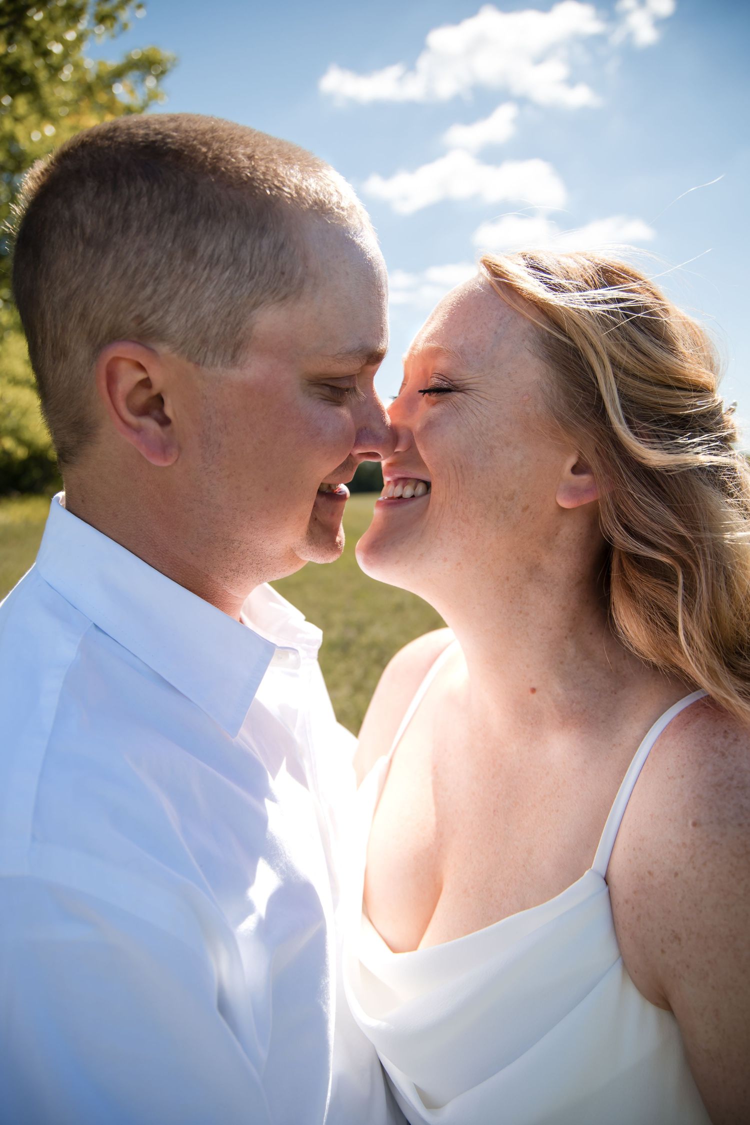 An intimate wedding portrait shows a couple sharing a romantic moment against a bright blue sky.