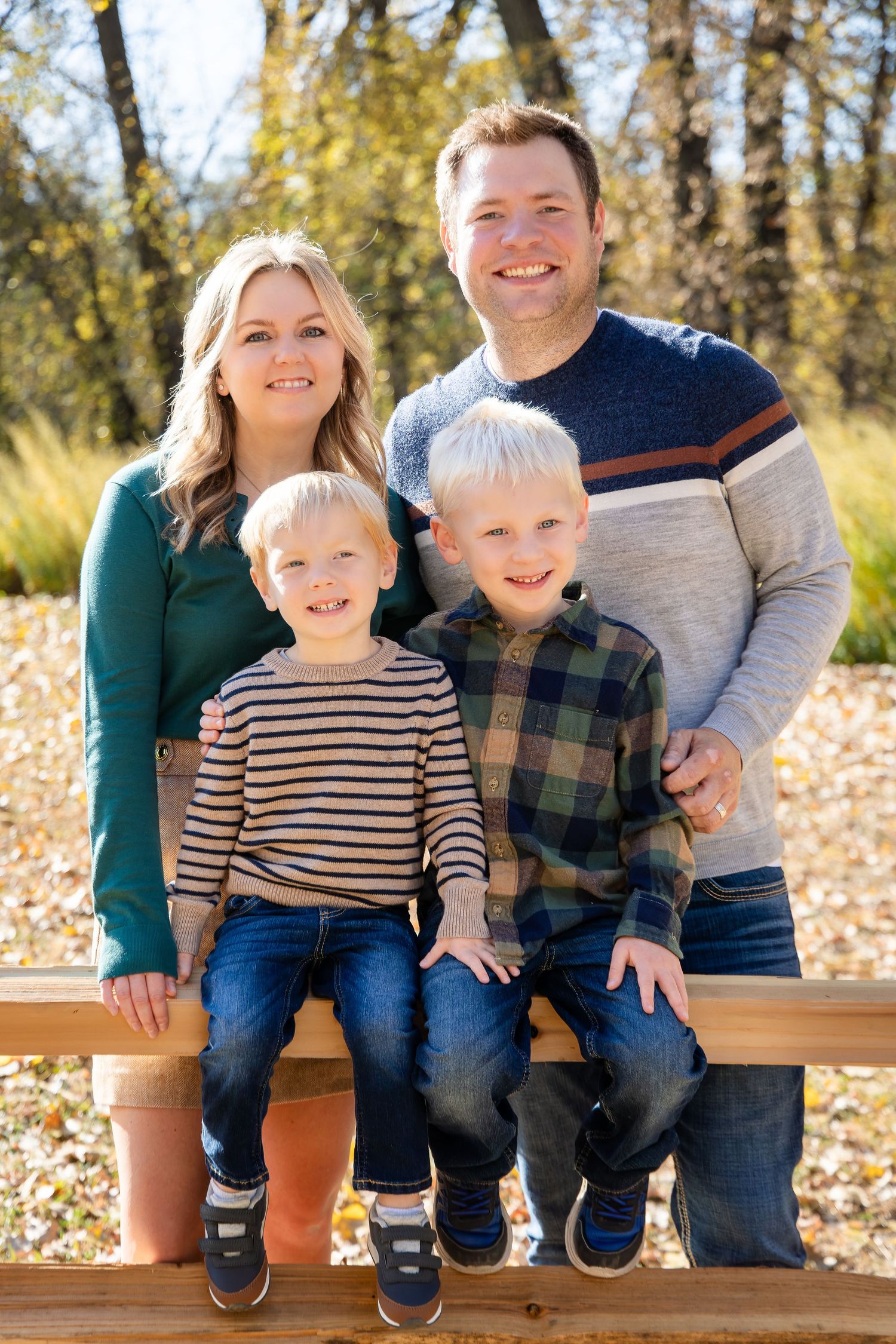 Family photo session on wooden bench with fall foliage in background.