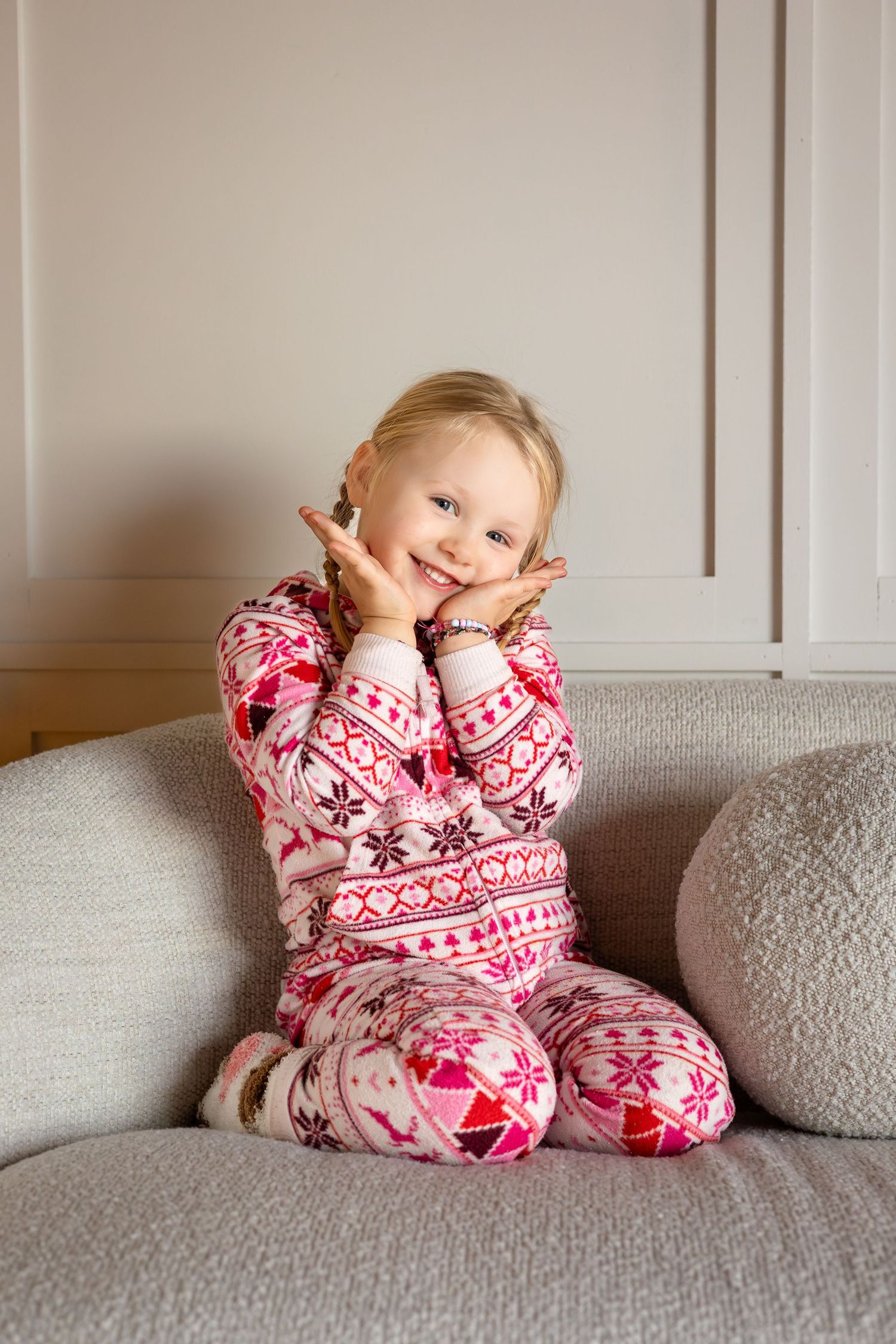 Playful poses in festive pink pajamas on a light gray couch.