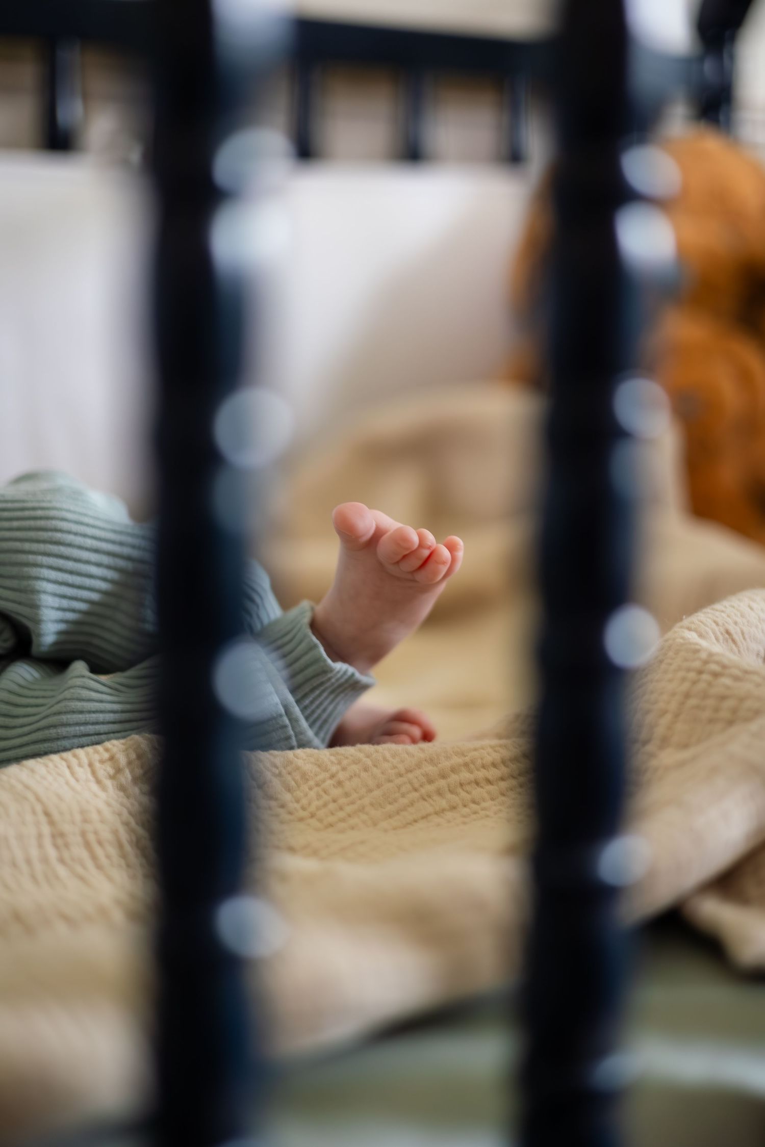 Small baby feet visible through crib bars with textured blanket.