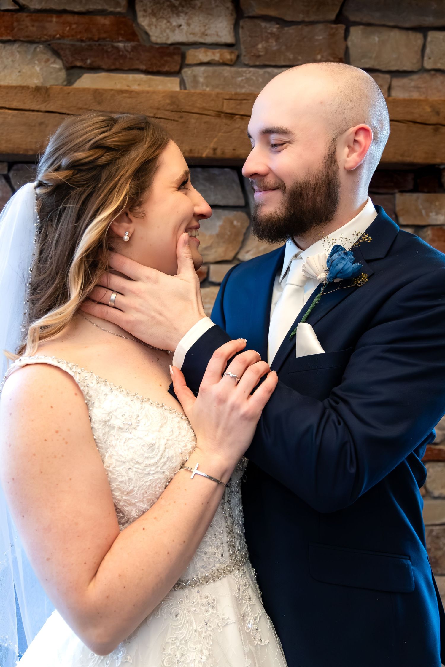 Bride and groom share a tender moment, gazing into each other's eyes near a stone wall.