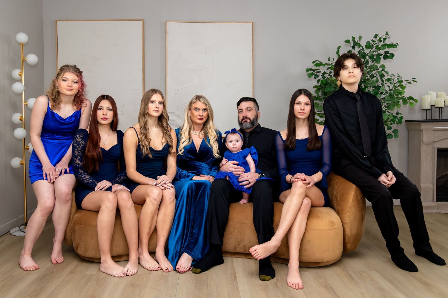 Family portrait of seven people in elegant blue and black outfits seated on a sofa in a modern interior.