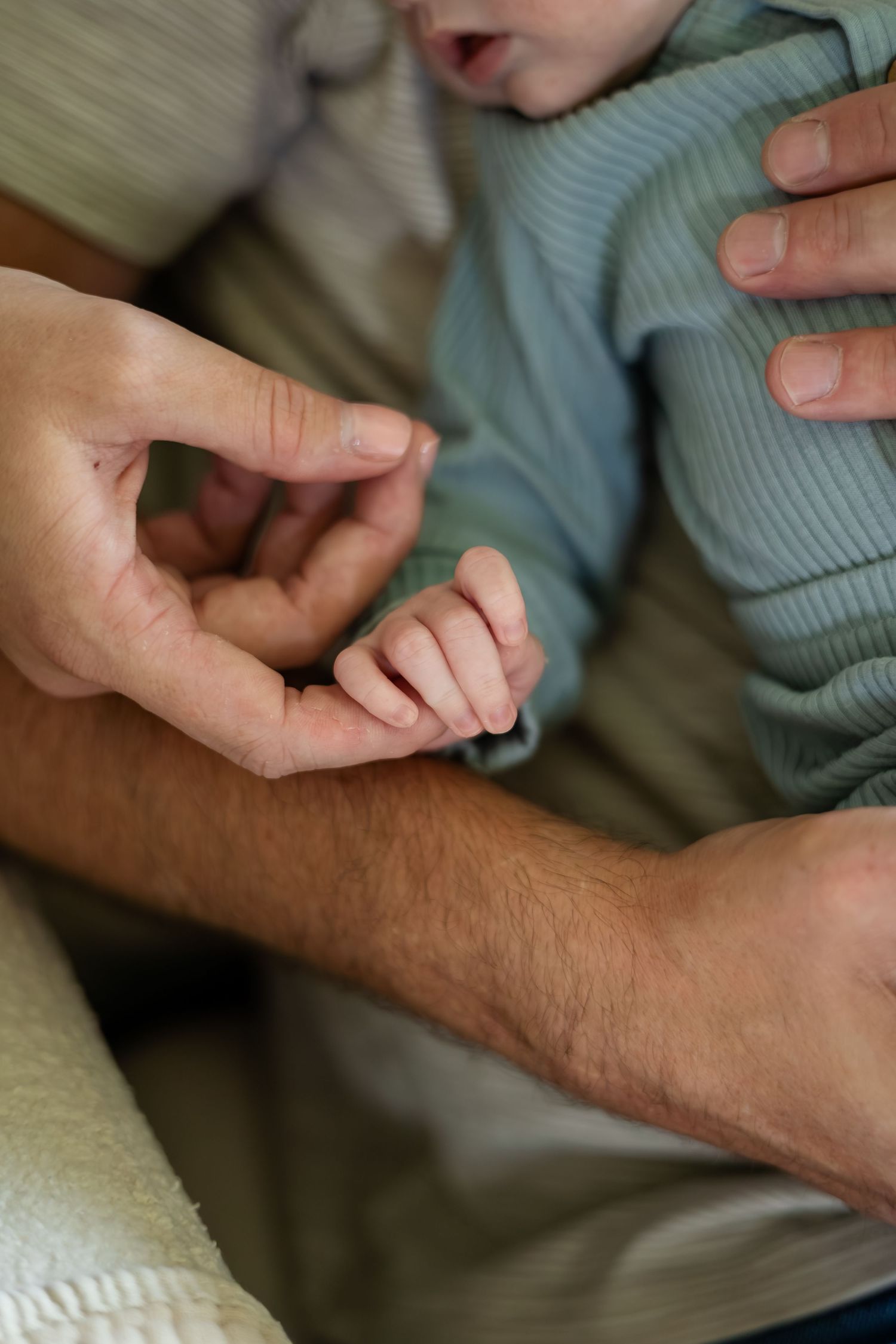 Close-up of hands gently holding baby's tiny fingers.