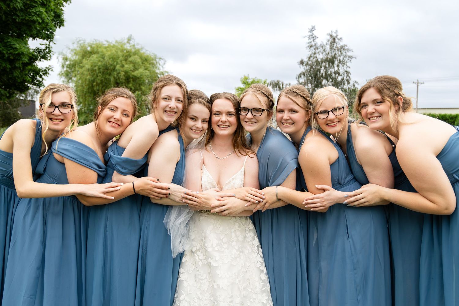 Wedding party in blue bridesmaid dresses poses playfully with the bride.