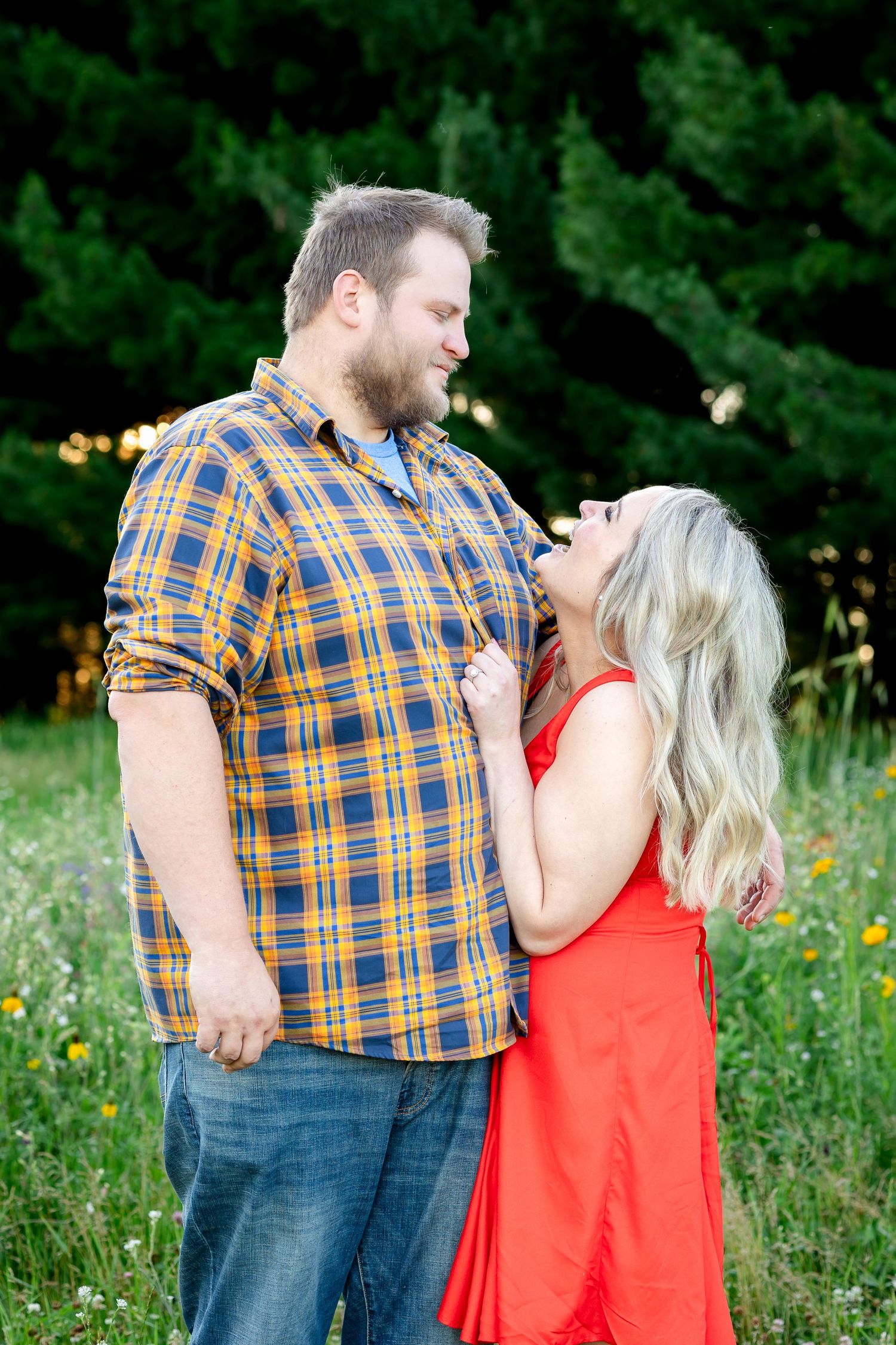 A couple in a plaid shirt and red dress share an intimate moment in a wildflower field.