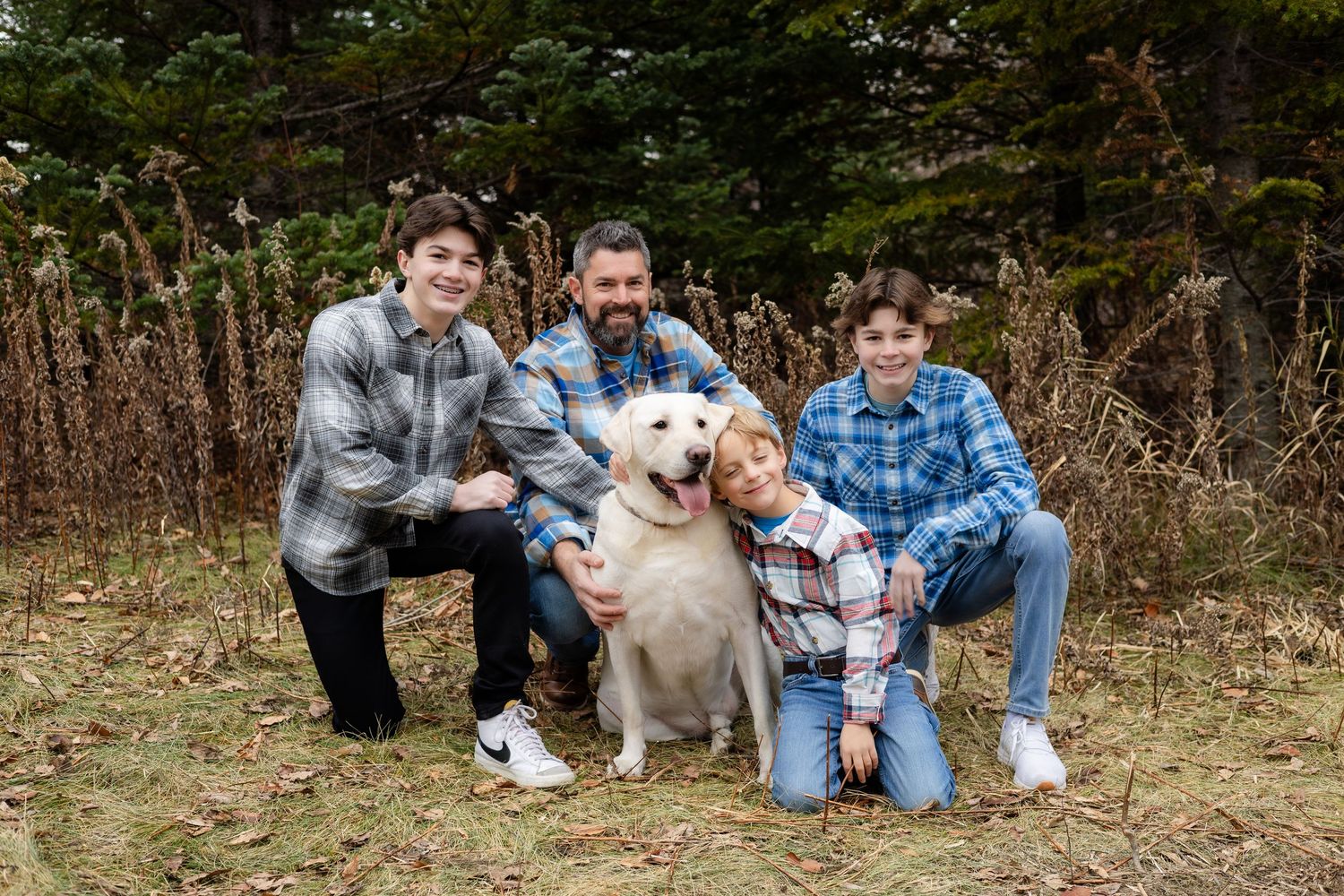 A group photo featuring a white dog and people in coordinated plaid shirts outdoors.