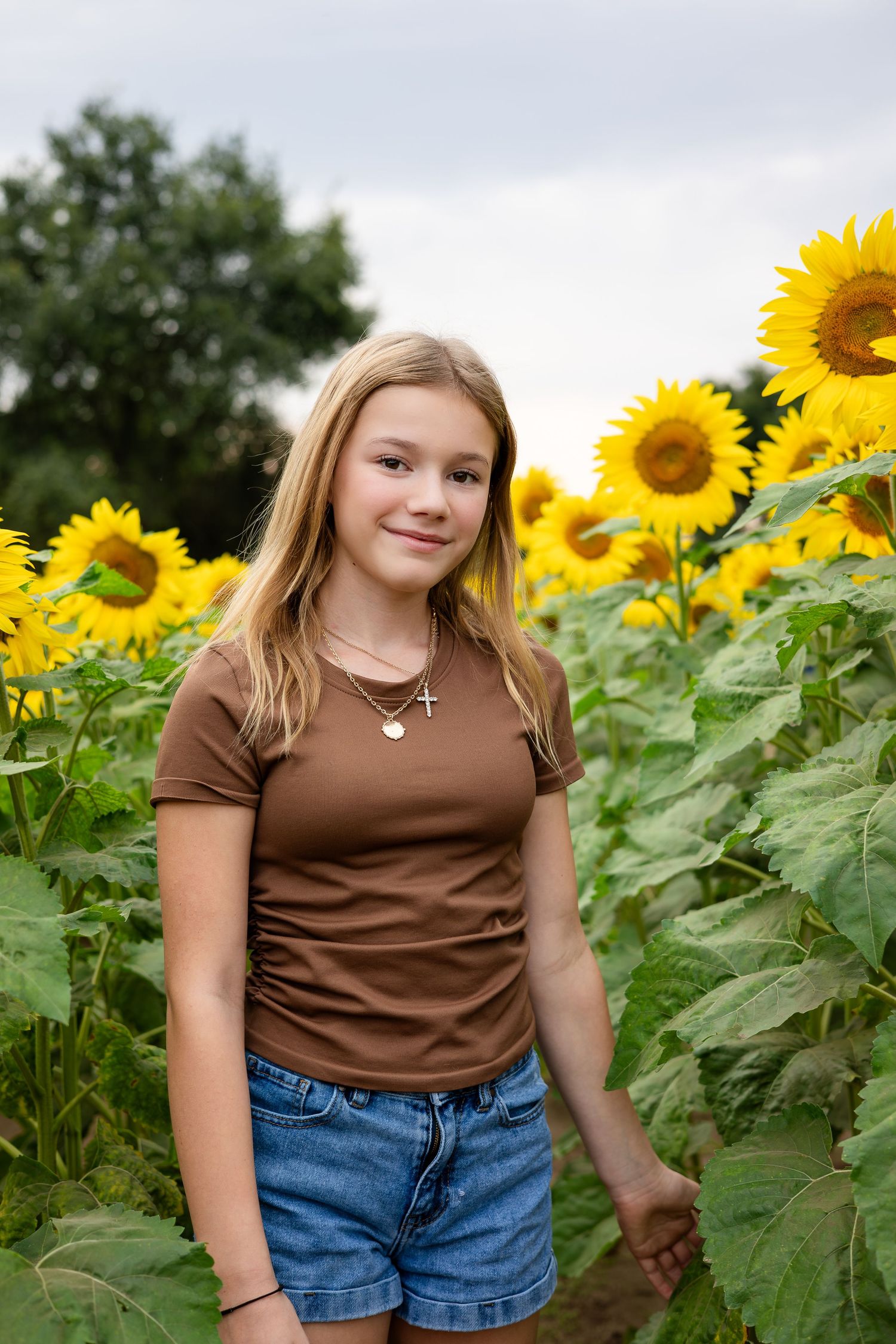A person in a brown shirt stands among blooming sunflowers in a summer field.