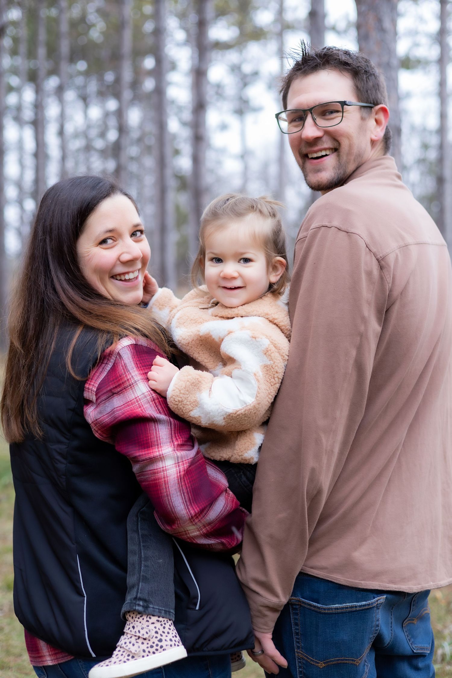 A happy family of three shares a warm embrace in a forest setting.