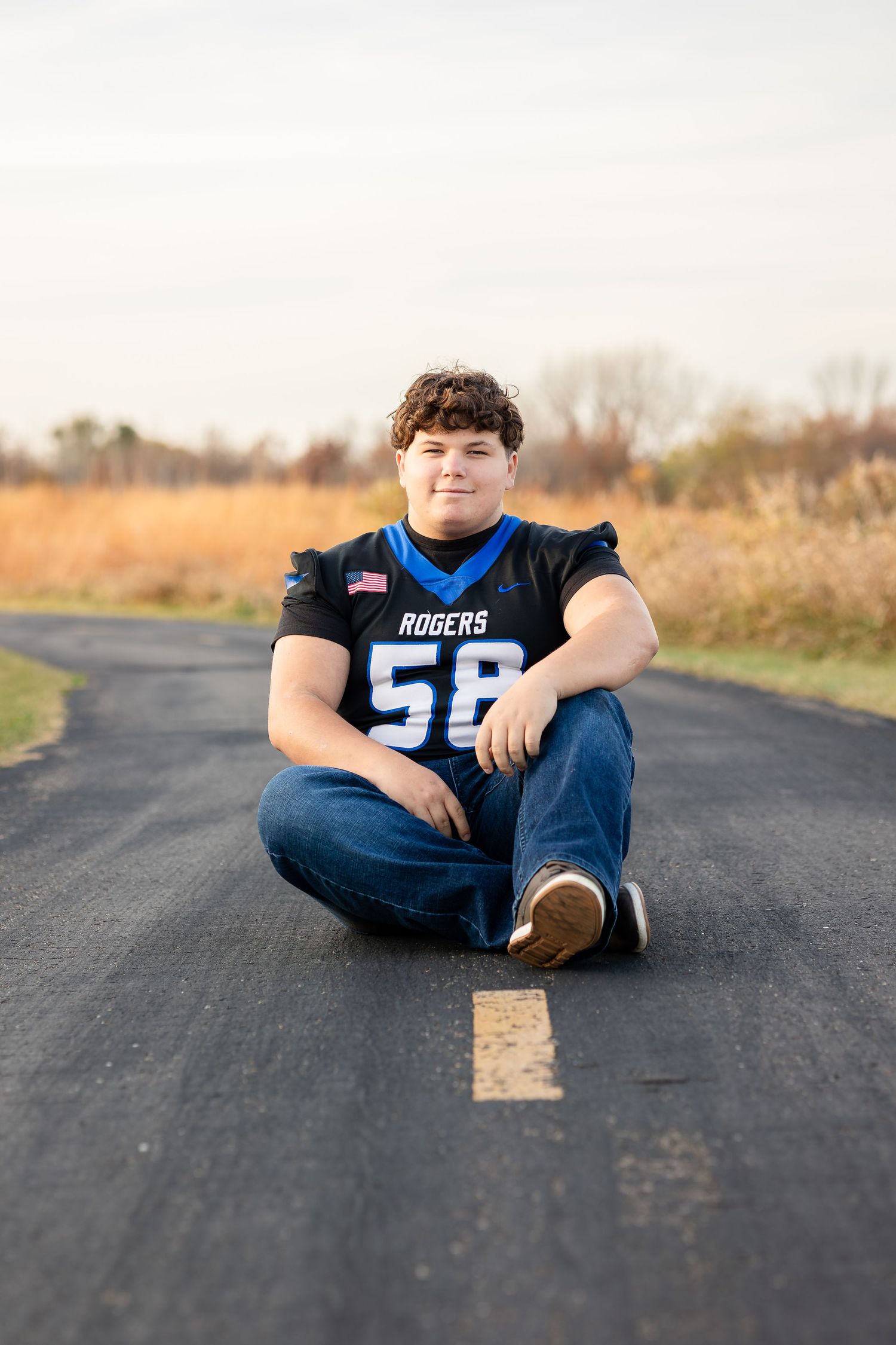 Person in sports jersey sitting on asphalt road during sunset.