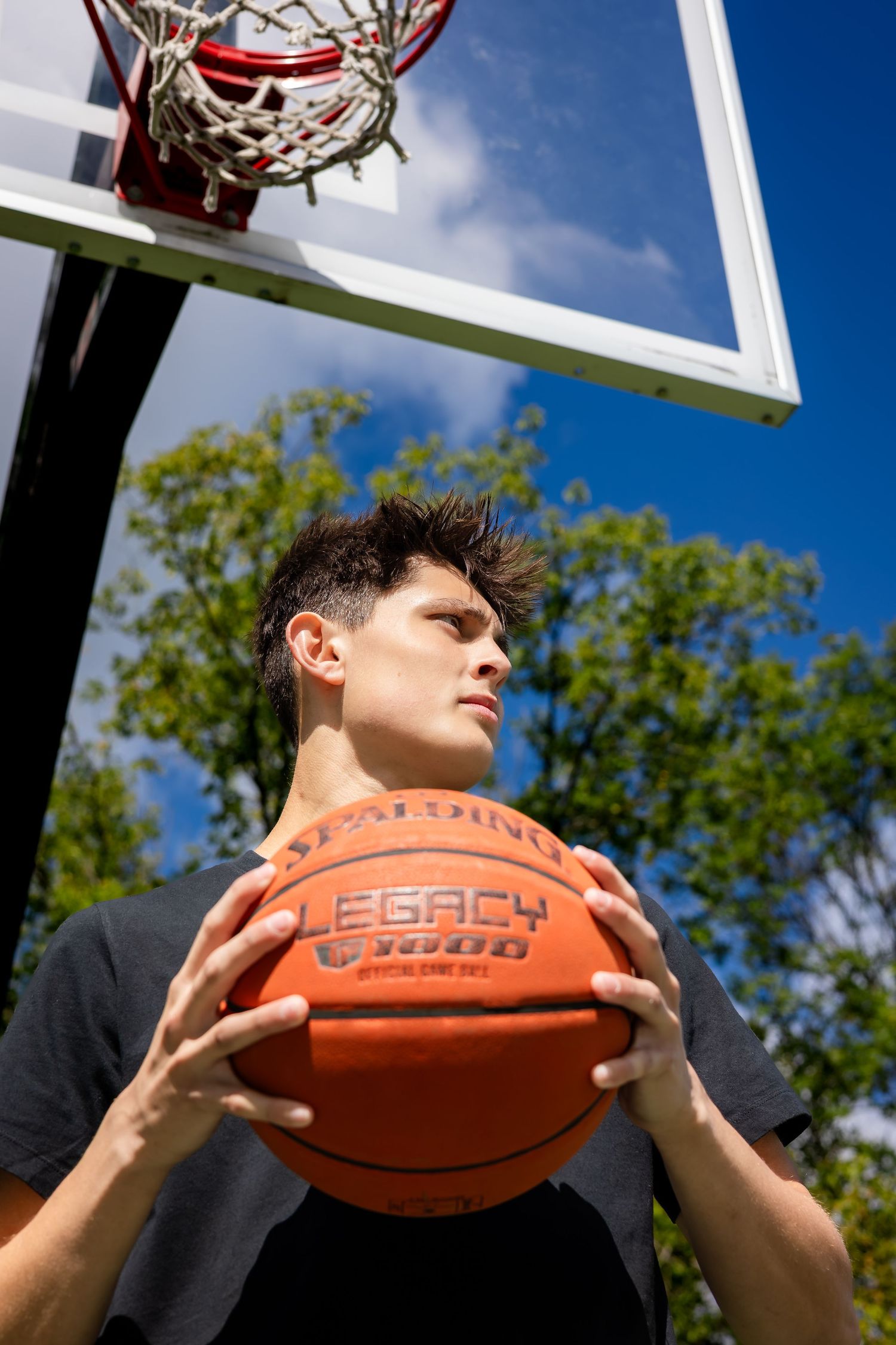 Close-up shot of basketball player holding orange ball against blue sky.