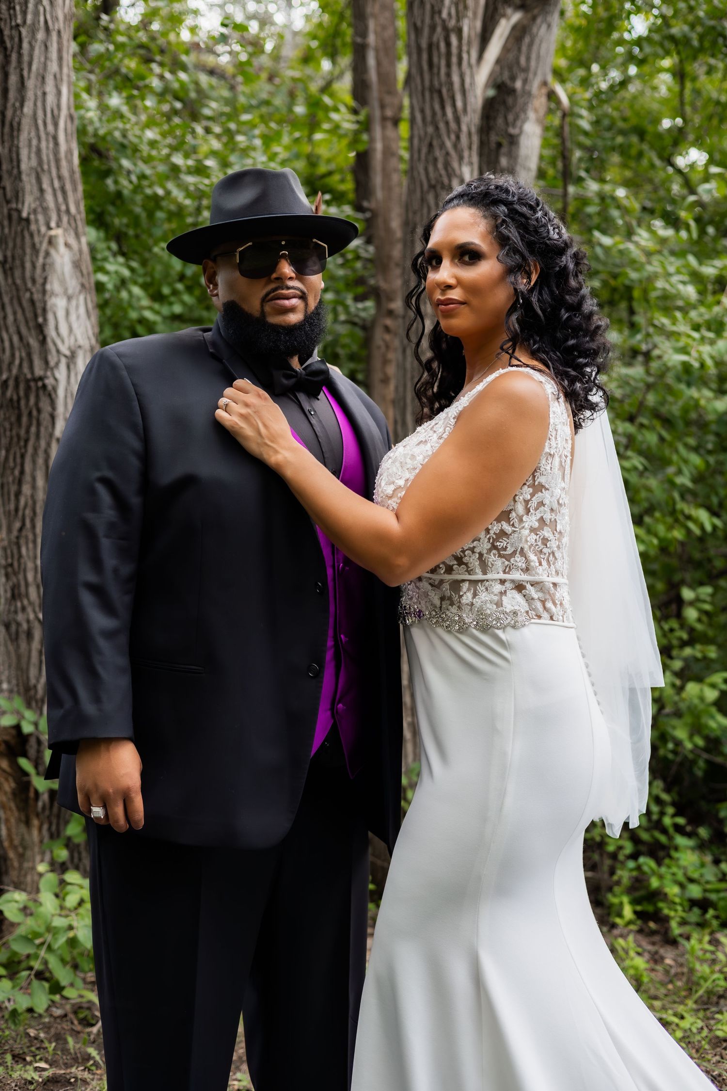 Newlyweds in formal attire share romantic moments among trees.