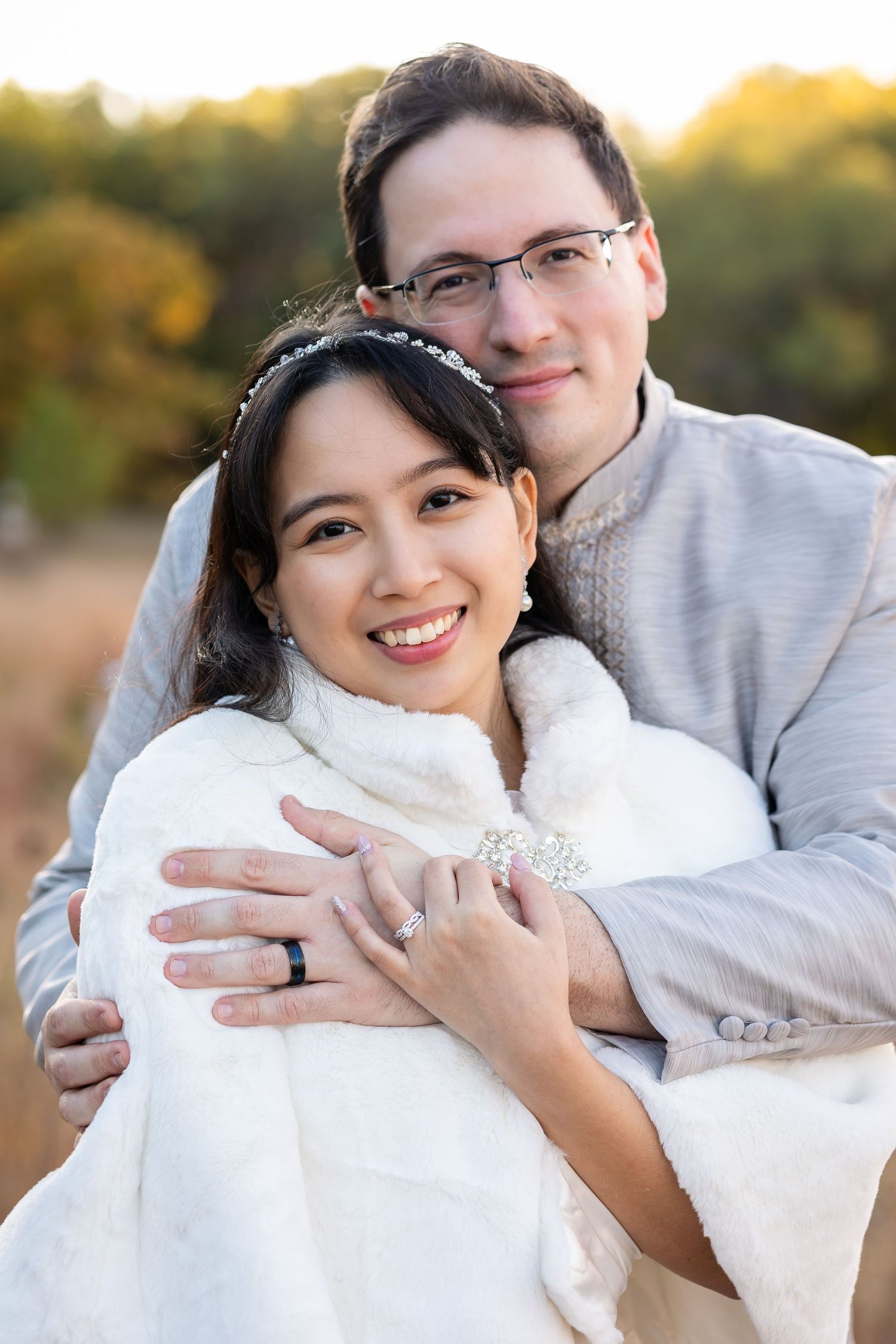 Couple in wedding attire holding and cuddling with a small white dog during an outdoor sunset photoshoot.