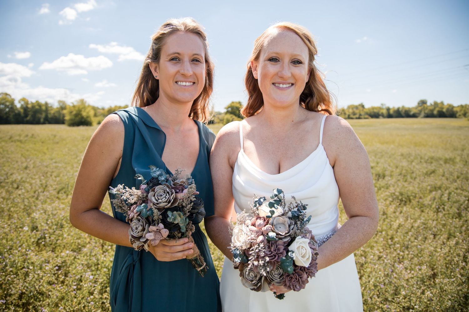 Wedding party members pose together in a sunny field with floral bouquets.