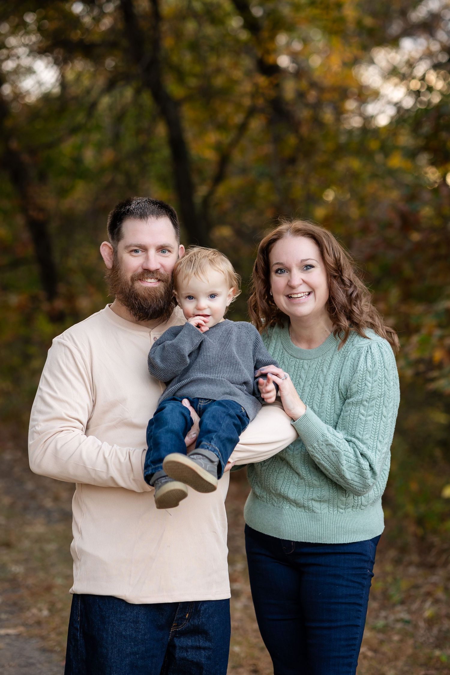 Family wearing coordinated outfits posing in autumn forest setting.
