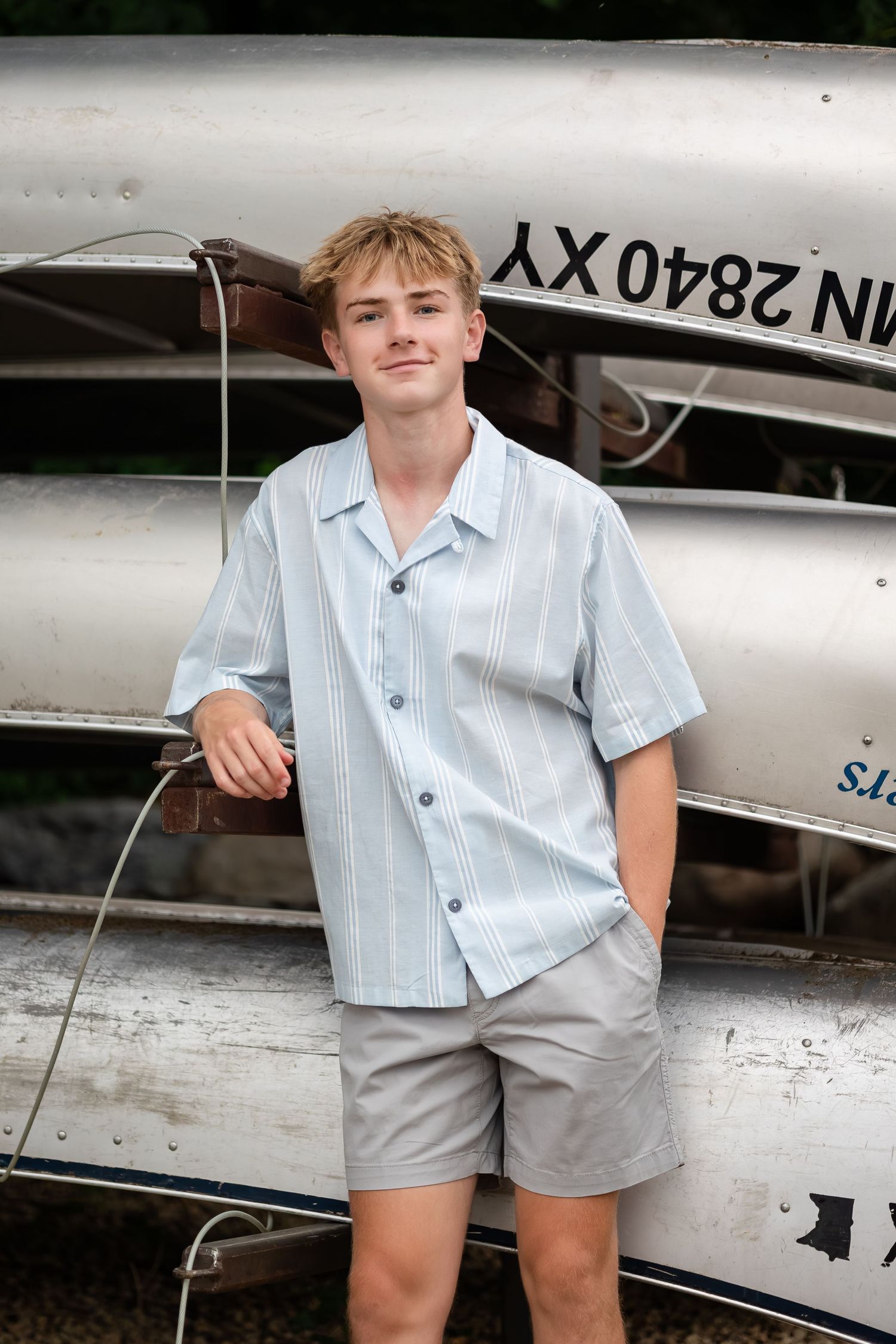 Person in light shirt poses casually next to stacked canoes with registration numbers.