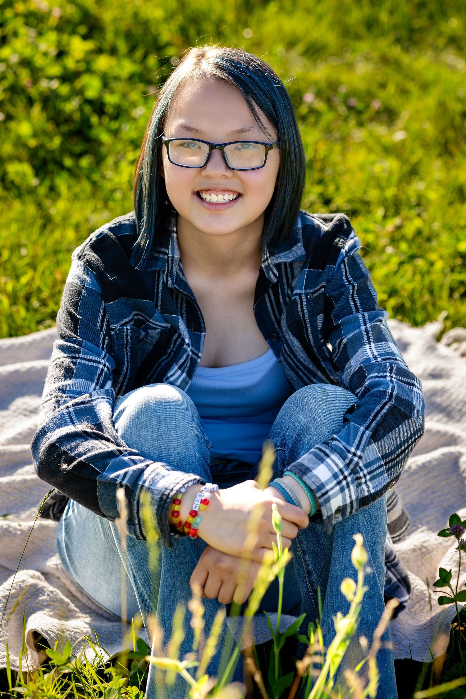 Person sitting on rocks wearing plaid flannel and jeans in sunny outdoor setting.