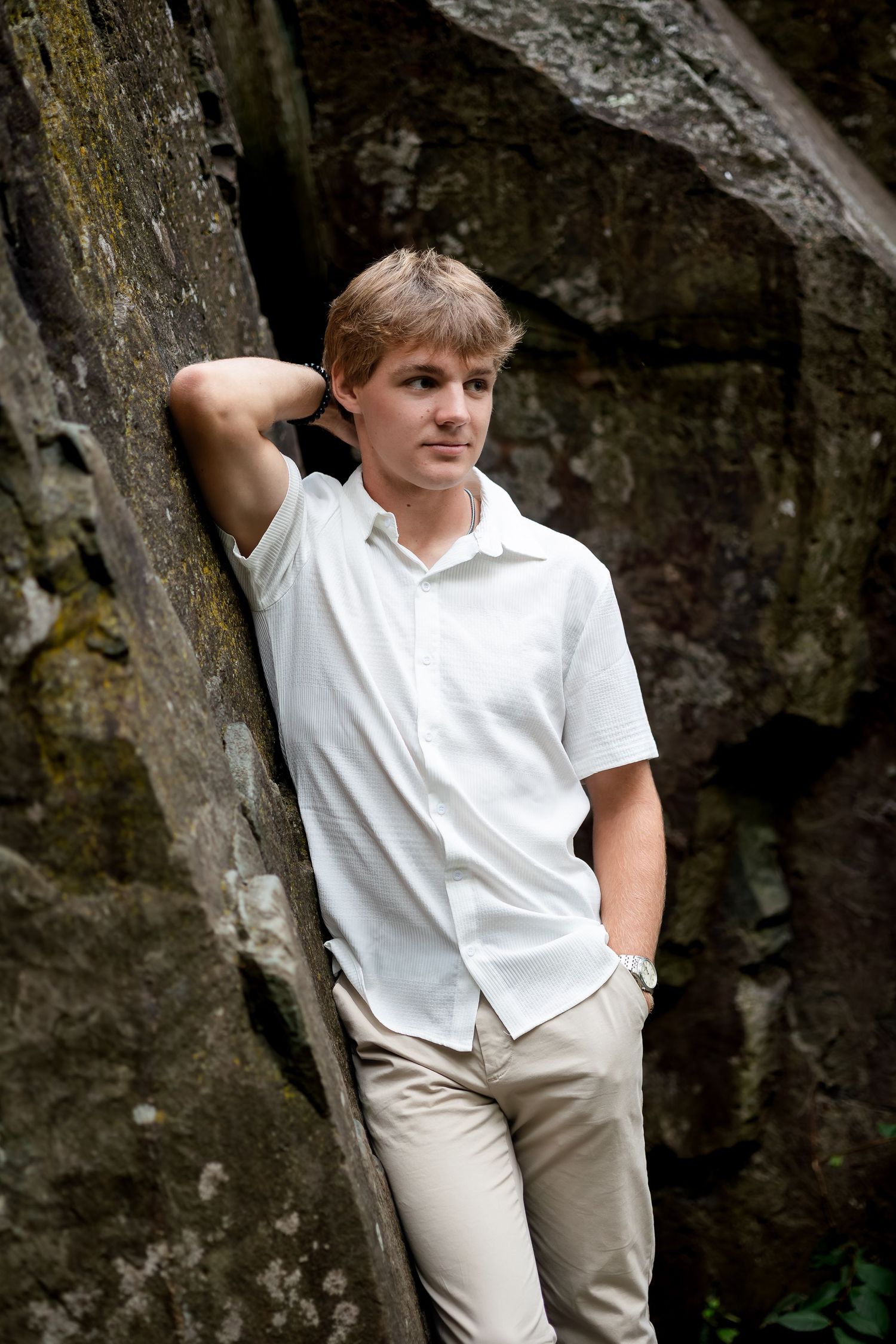 Figure in white shirt poses against dark rock wall in casual outdoor portrait.