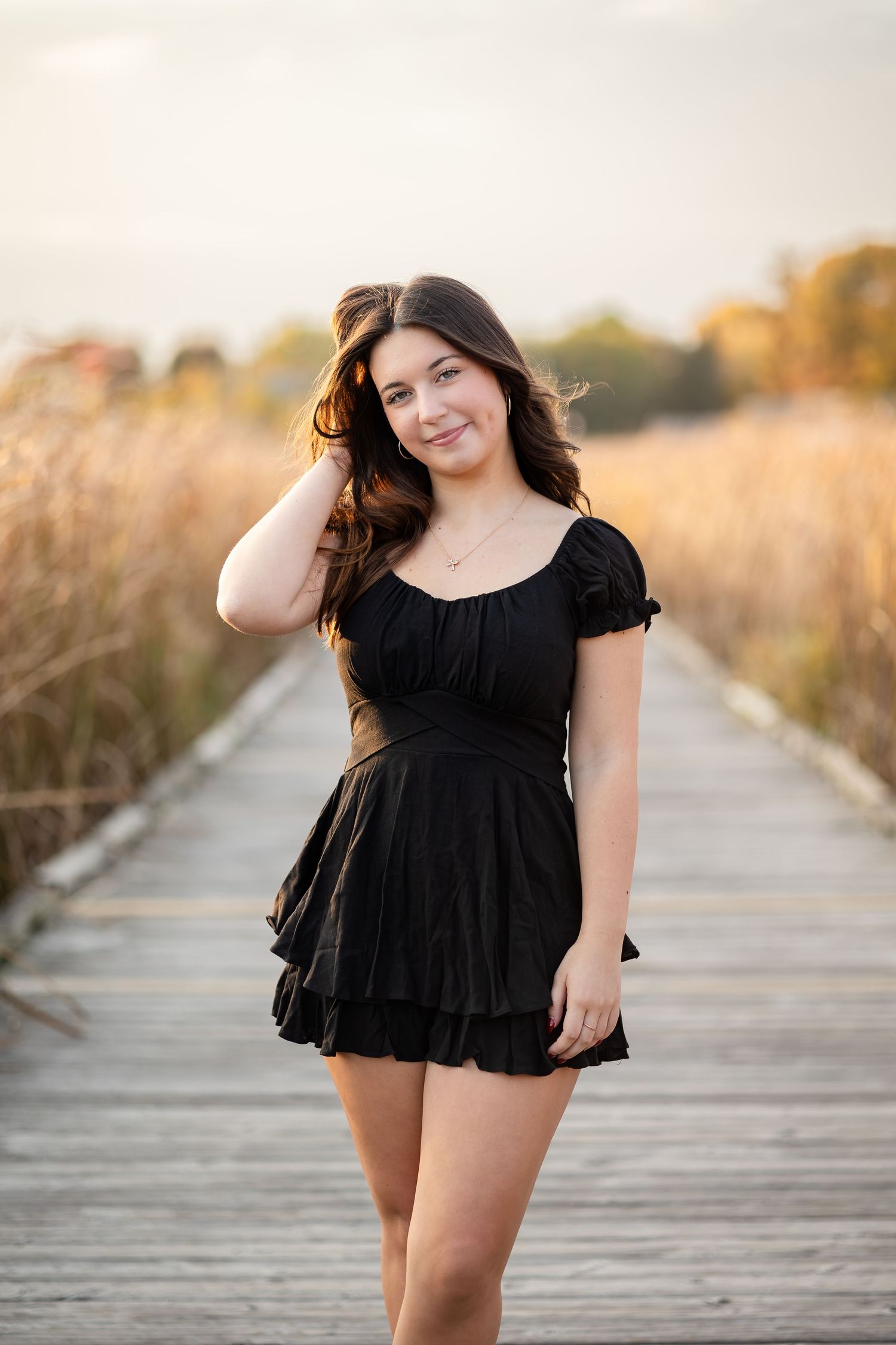 Playful poses in black dress on wooden boardwalk at sunset.