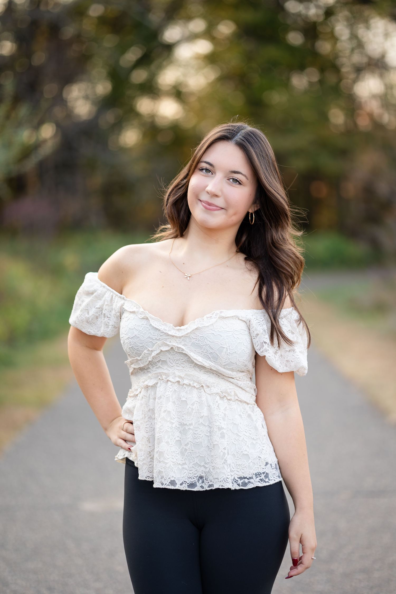 Outdoor portrait on path wearing white lace top and black pants.
