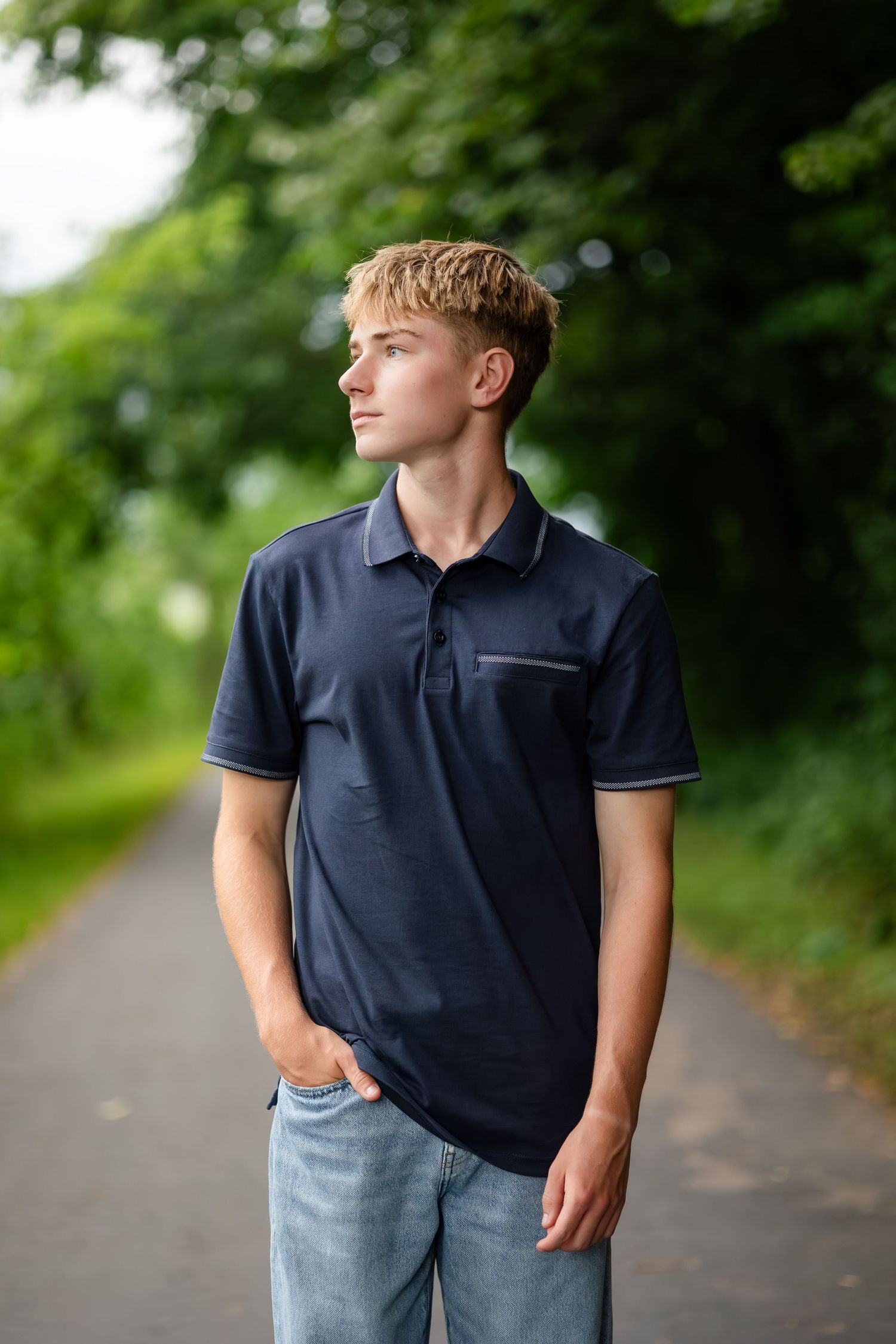 Portrait series of person in navy polo shirt on tree-lined path.