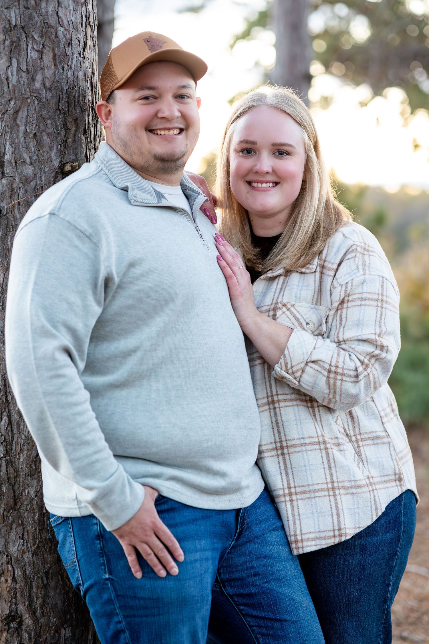 A couple poses together against a tree trunk in casual attire during an outdoor photo session.