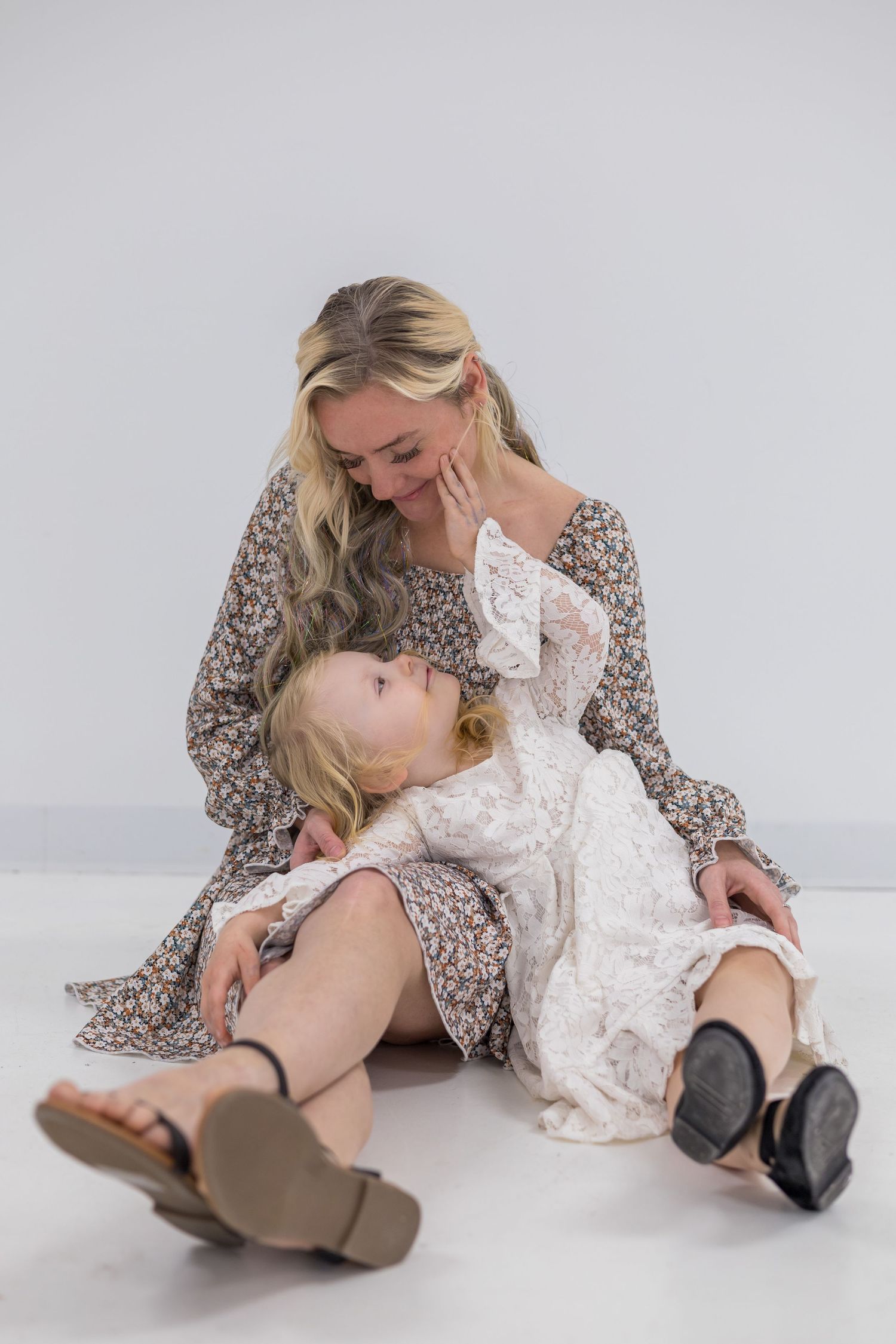 An intimate moment between parent and child wearing coordinating floral dresses on a white background.
