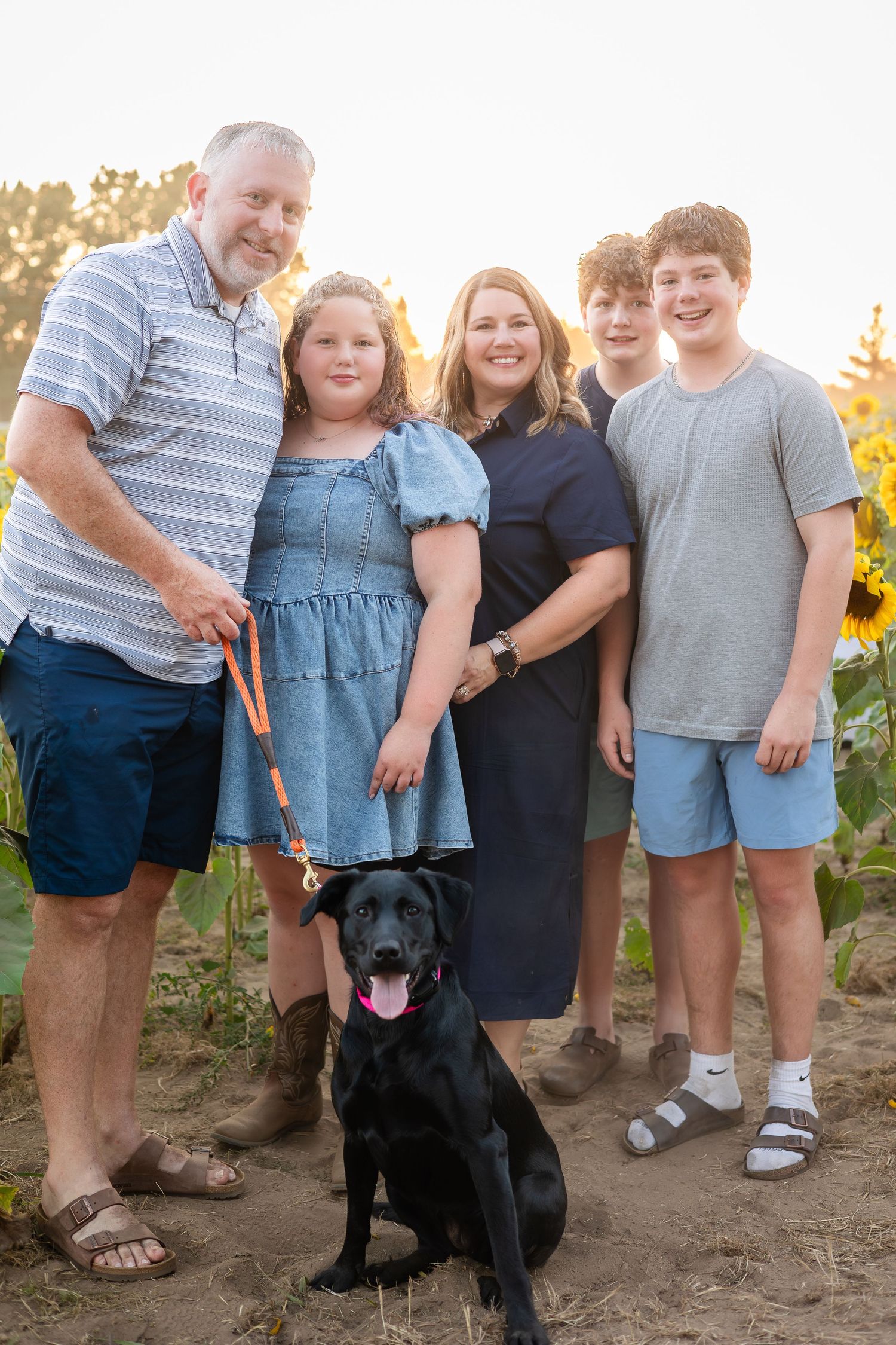 Group photo with black dog in sunflower field during golden hour.