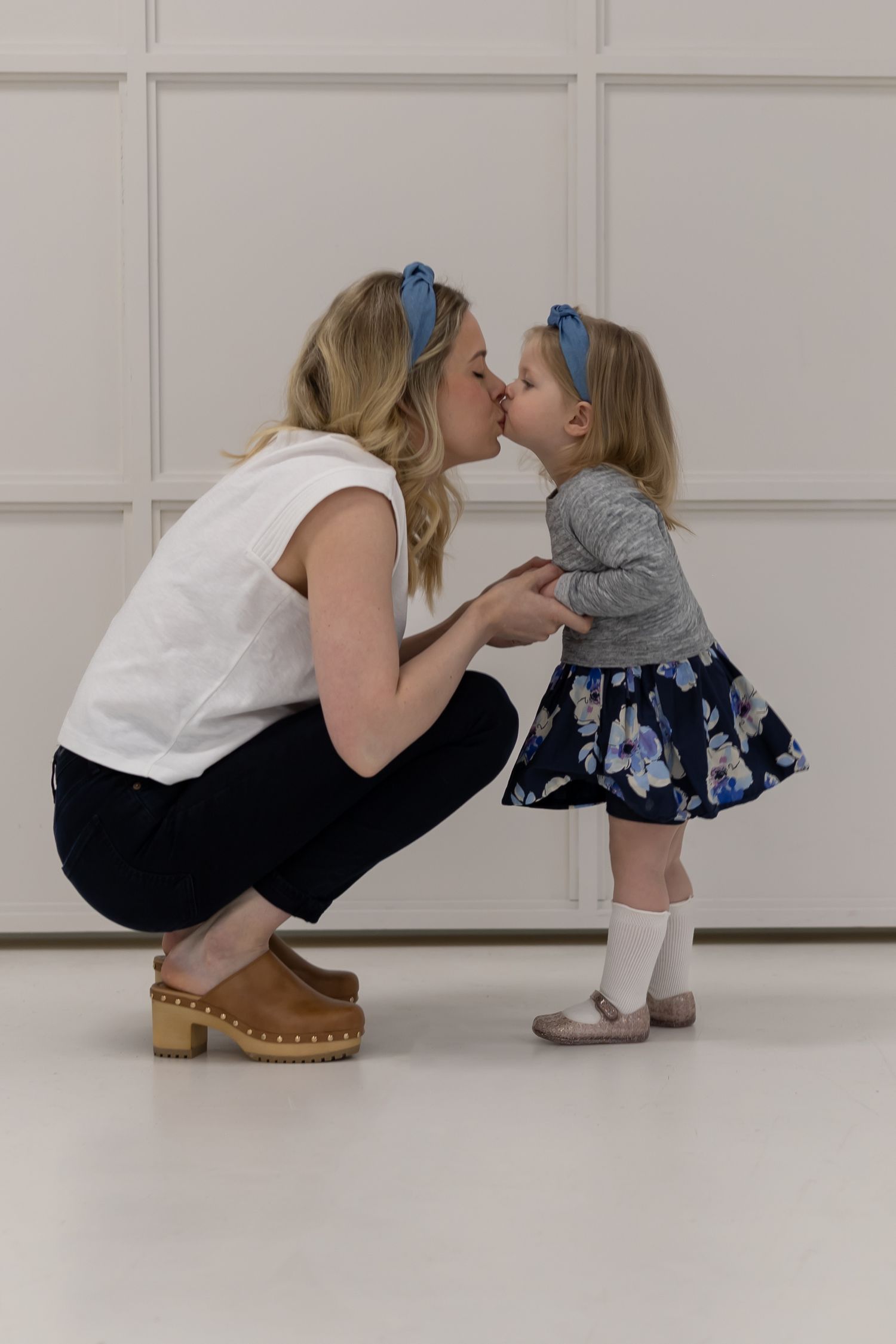 A tender moment captured against a white wall as matching blue headbands create a sweet coordinated look.