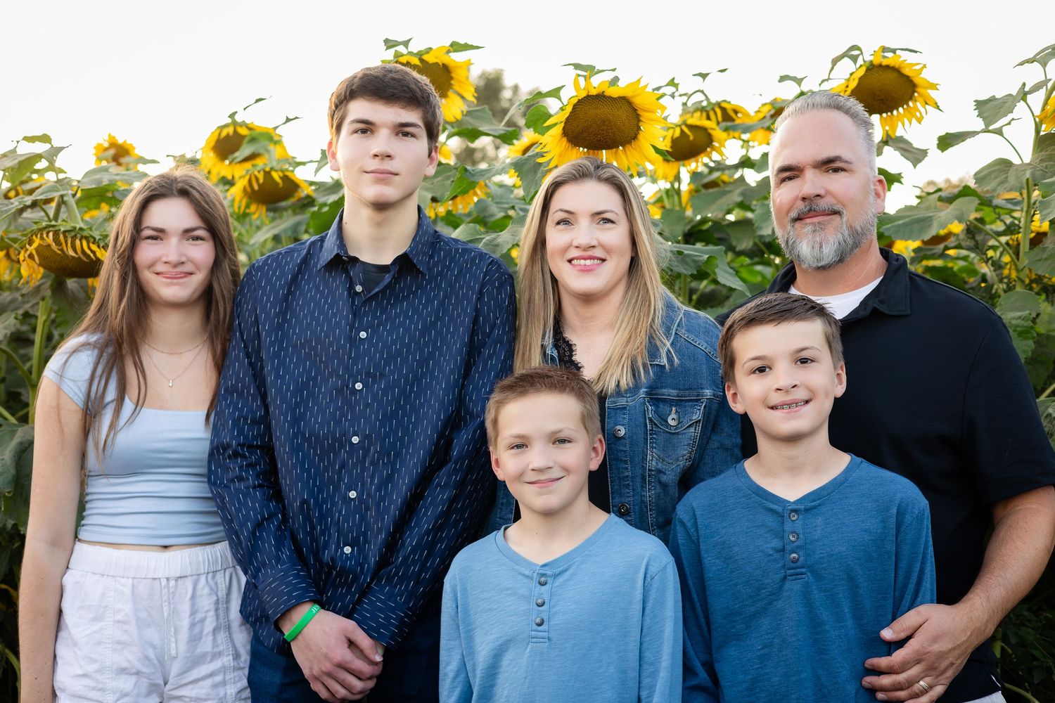 A group portrait of family members wearing coordinated blue and black outfits in a sunflower field.