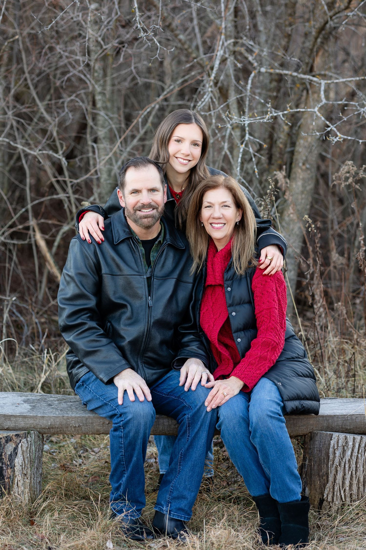 Family members sit together on wooden log bench during outdoor photo session.