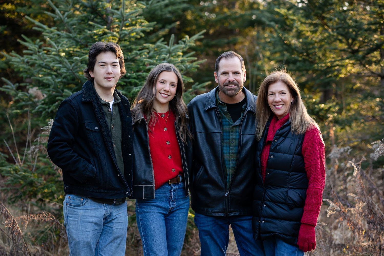 People in casual winter wear pose together against an evergreen forest backdrop.