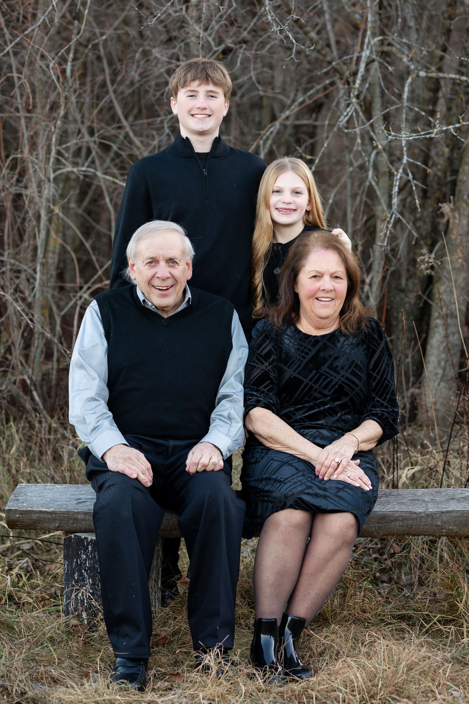 Family group sitting together on a wooden bench surrounded by winter foliage.