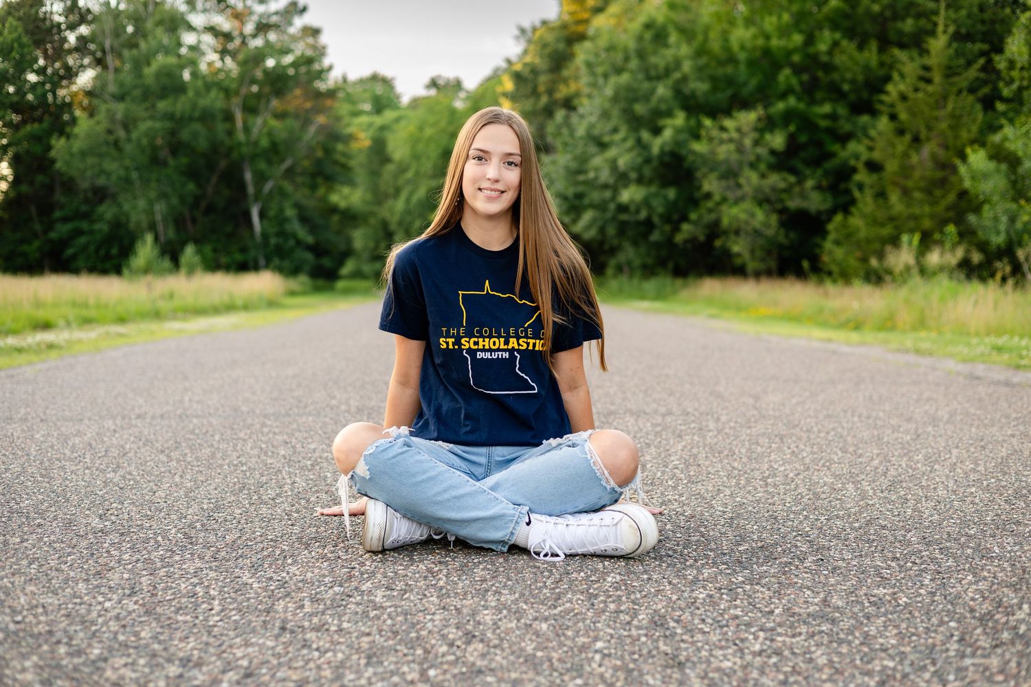 Person in casual attire sits cross-legged on asphalt road for outdoor portrait series.