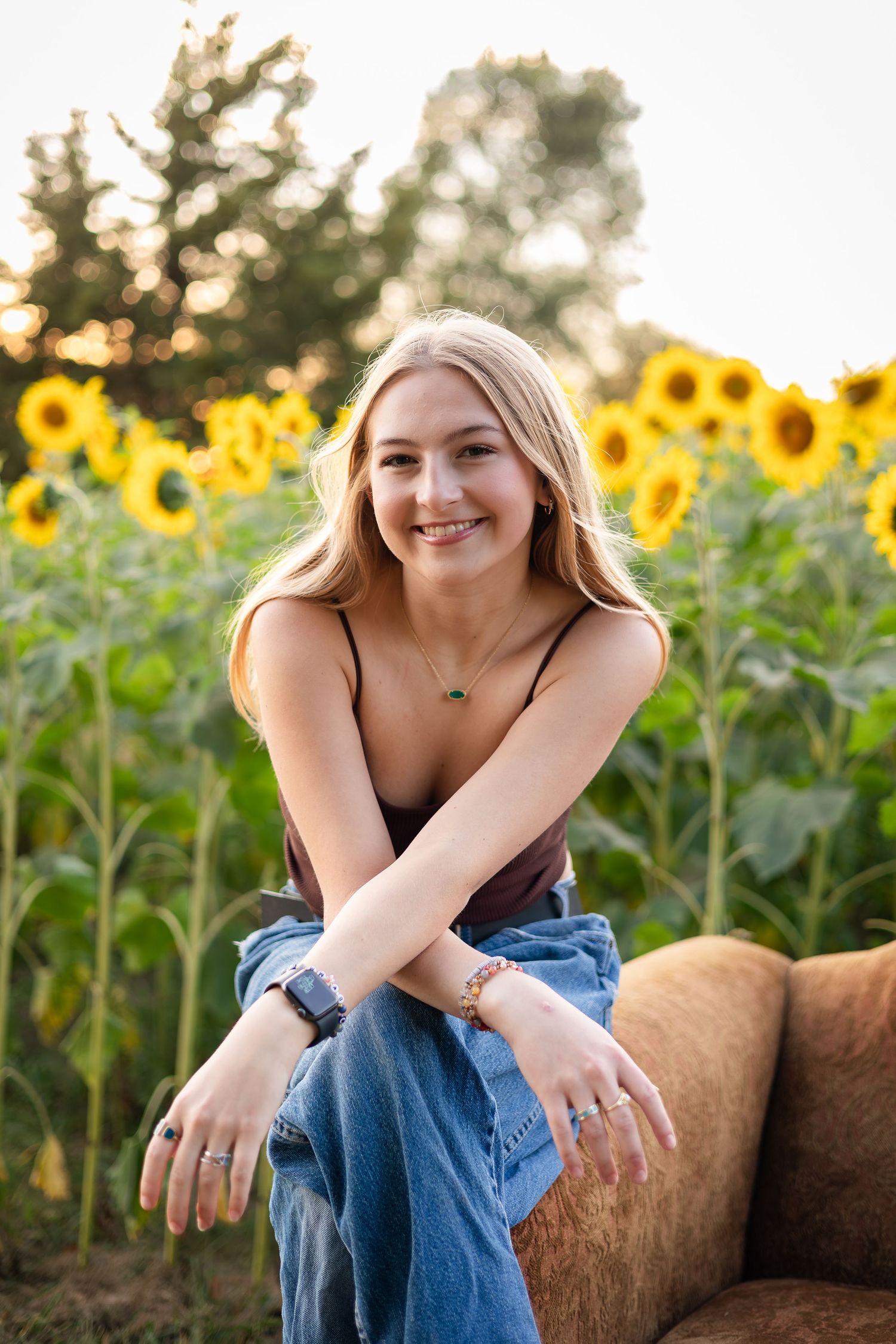 Woman relaxing on rustic bench in sunflower field during golden hour.