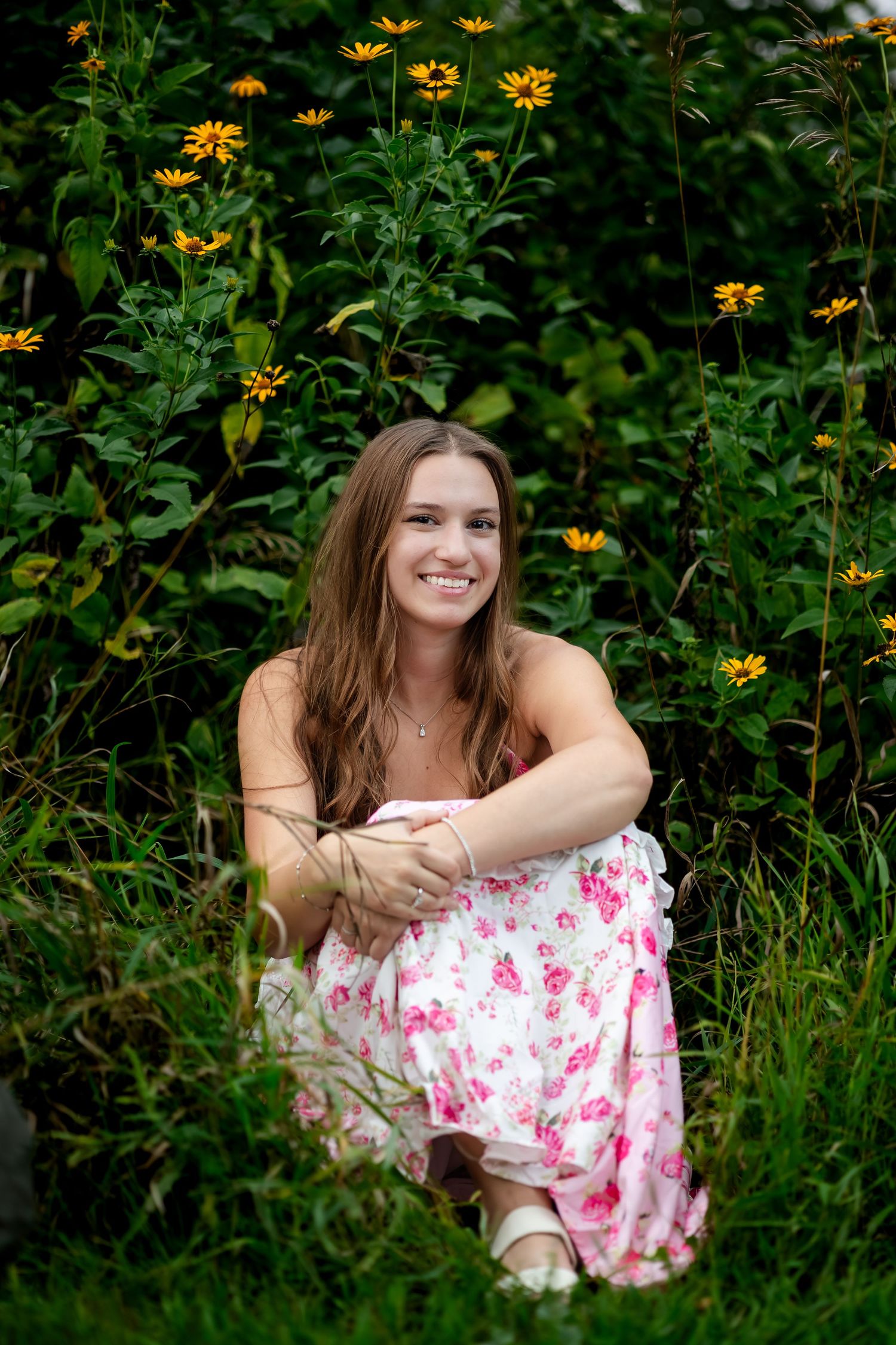 Person in floral dress relaxes among yellow flowers in lush garden setting.