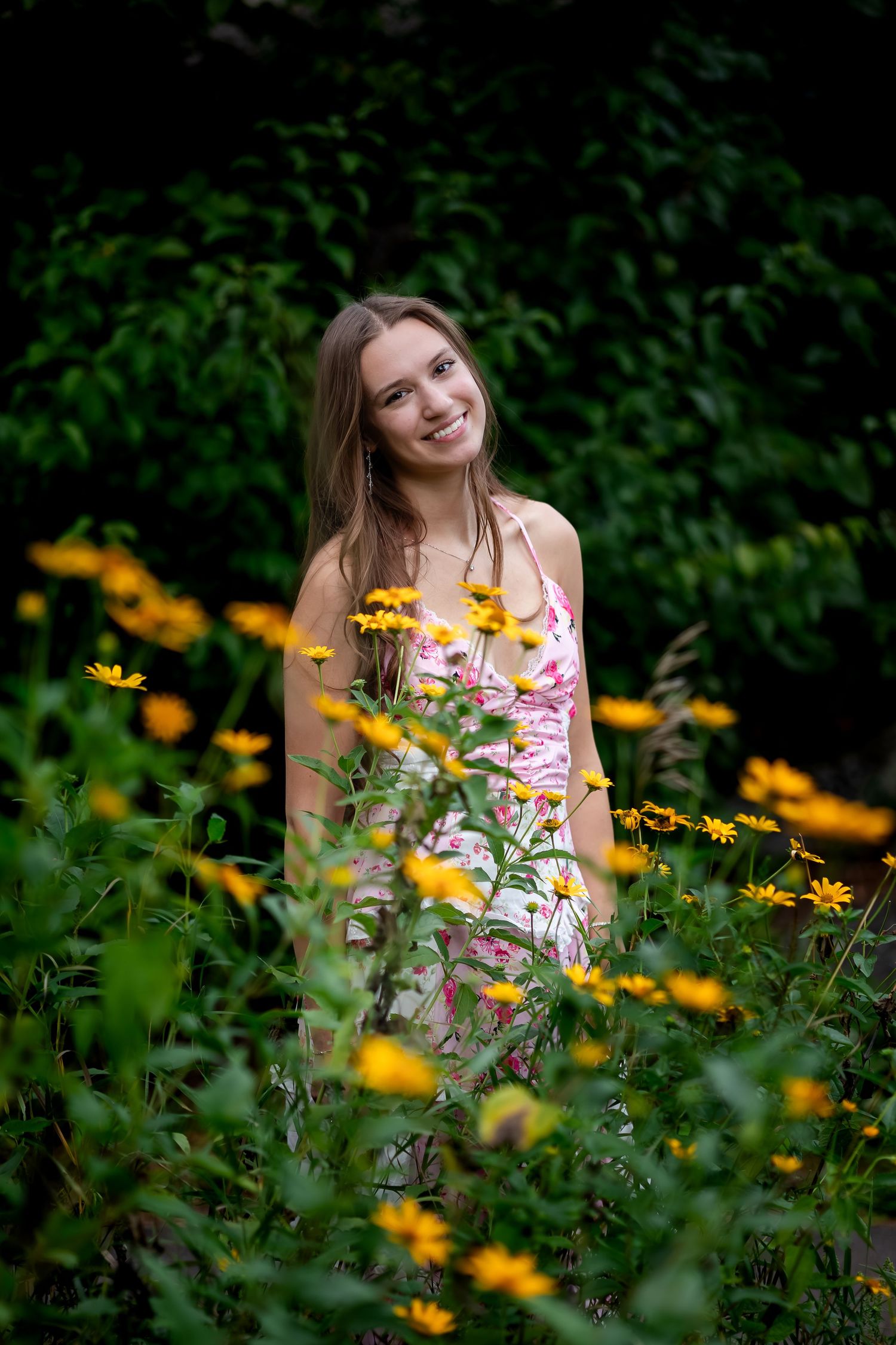 Person in floral dress poses among yellow wildflowers in garden setting.