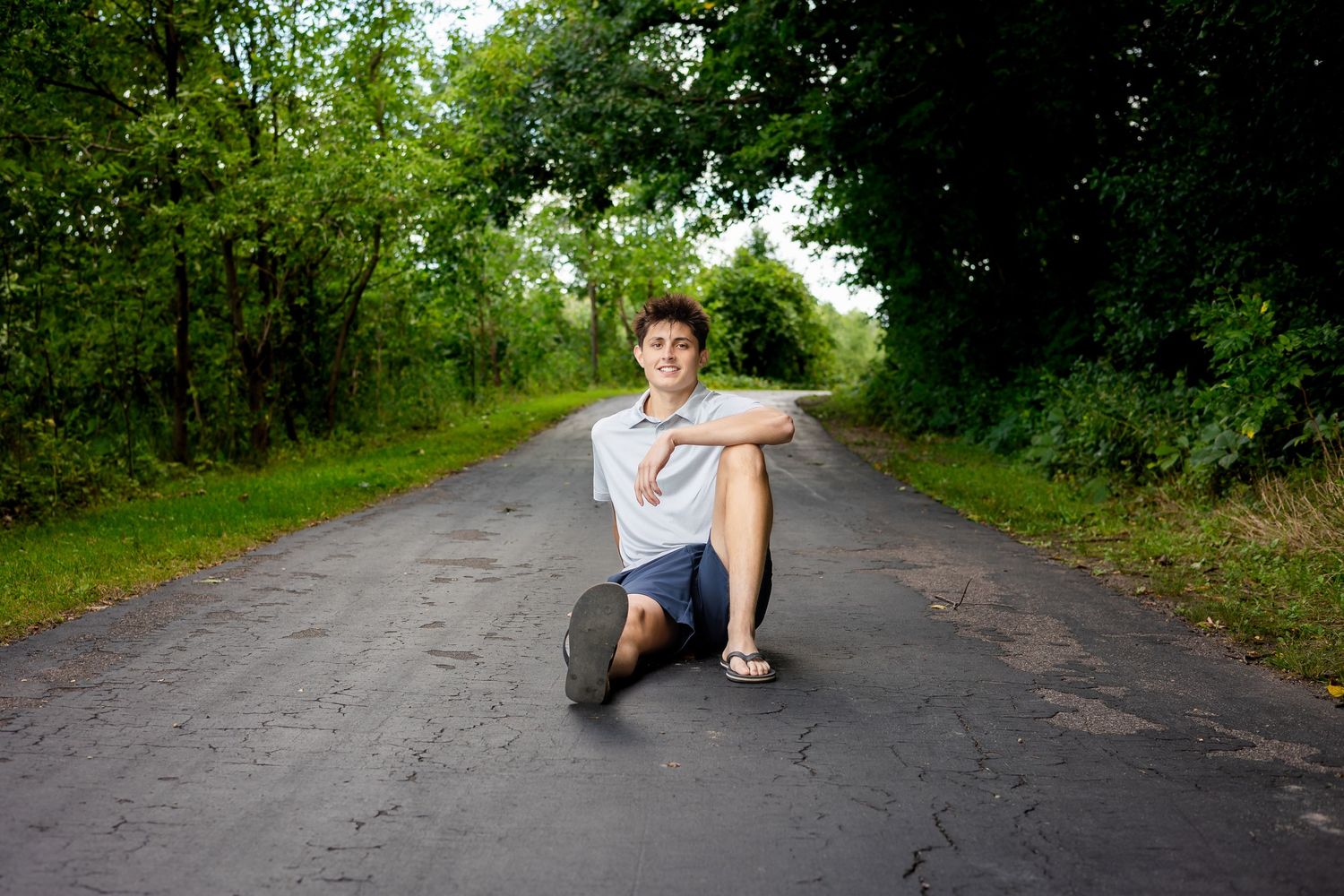 Person lounging on a paved pathway surrounded by green trees and foliage.