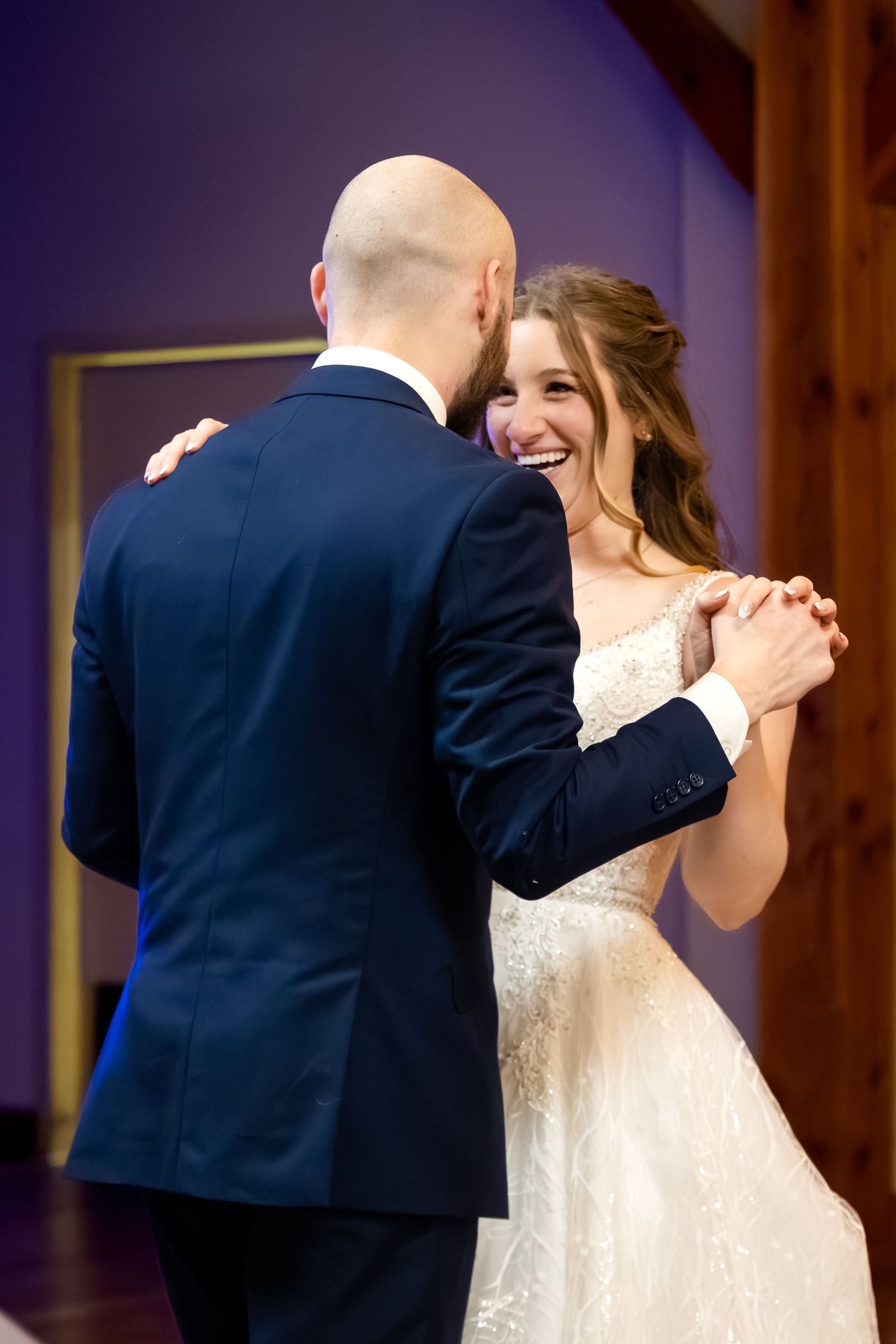 Bride and groom share their first dance, smiling joyfully in a warmly lit wedding reception venue.