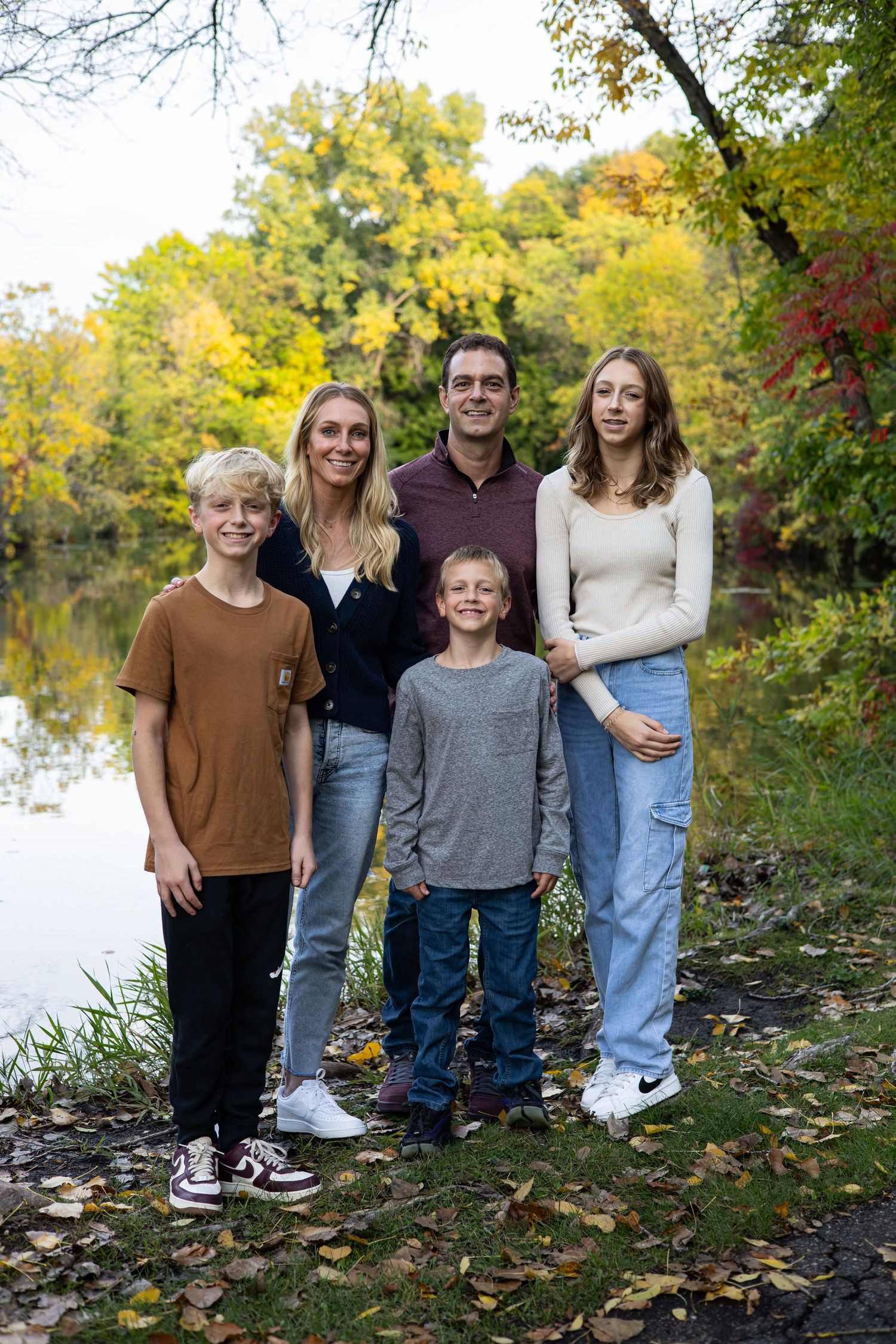 Family portrait by lakeside with fall foliage in background.